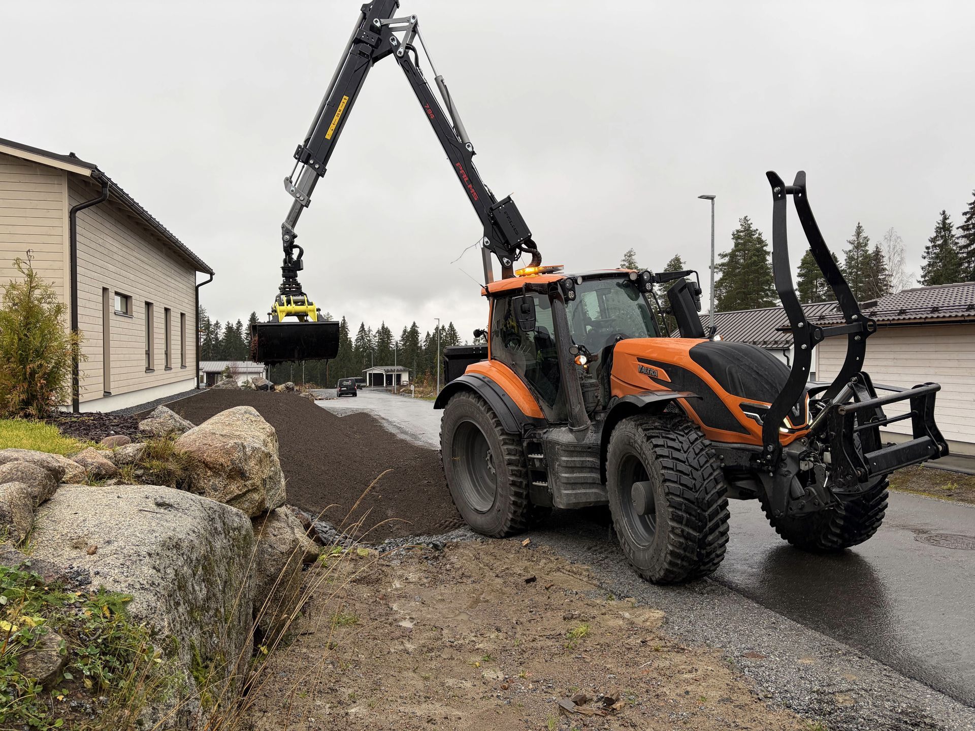 Vihreä traktori etukuormaajalla pysäköitynä sorakentälle laitteiden ja kuormalavojen viereen metsäalueella
