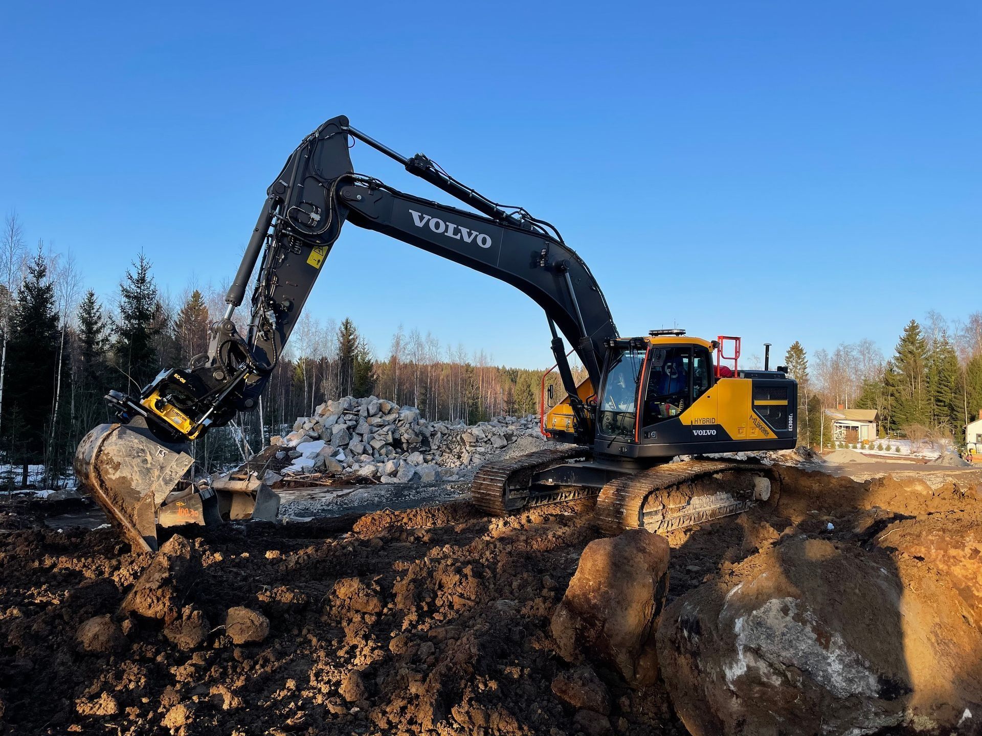 Musta Volvo-kaivinkone kaivaa mutaista aukiota sinisen taivaan alla