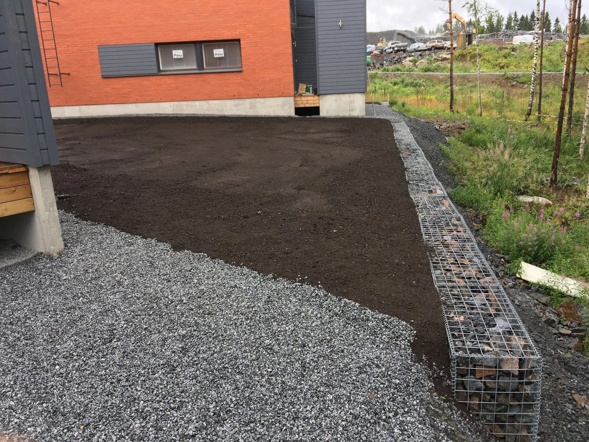 Tuore musta sorapolku tiilitalon vieressä, jossa on gabion-reunus ja puutarha-alue.