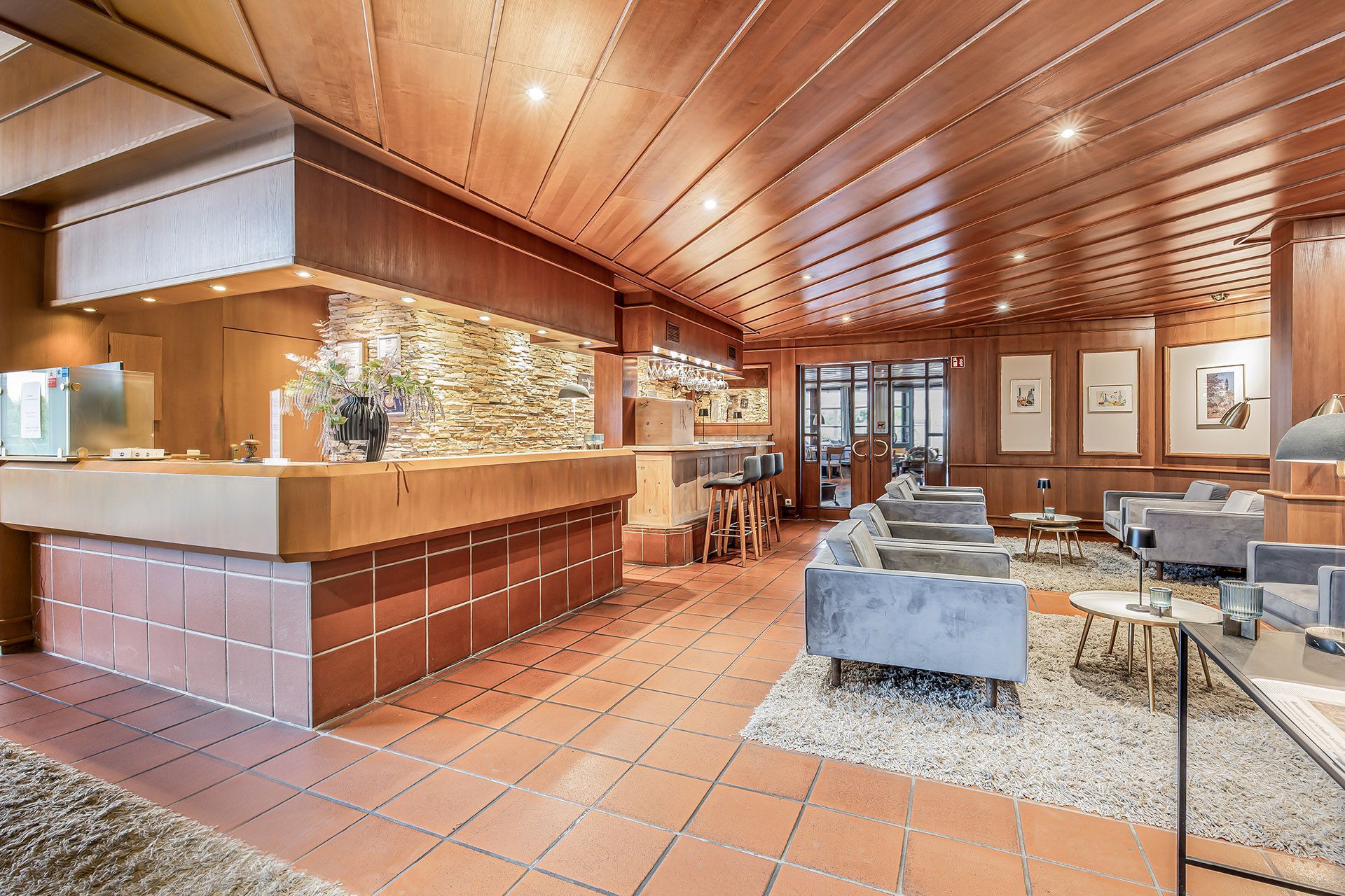 Hotellobby mit Holzvertäfelung, Fliesenboden, Sitzgelegenheiten und Rezeption.