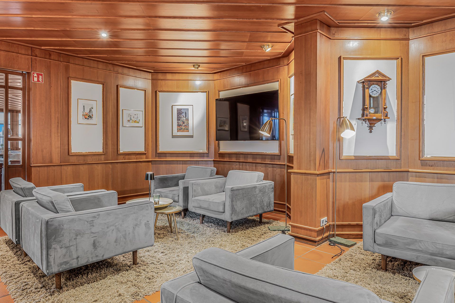 Hotellobby mit grauen Sofas, einem Teppich, Kunst, einem Fernseher und einer Standuhr.