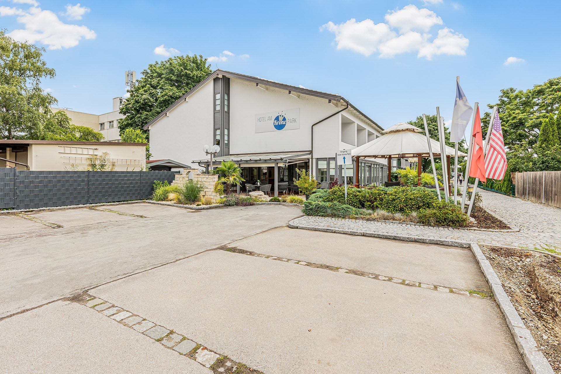 Außenansicht des Hotel am Krone Park mit Flaggen, Pavillon und Parkplatz an einem sonnigen Tag