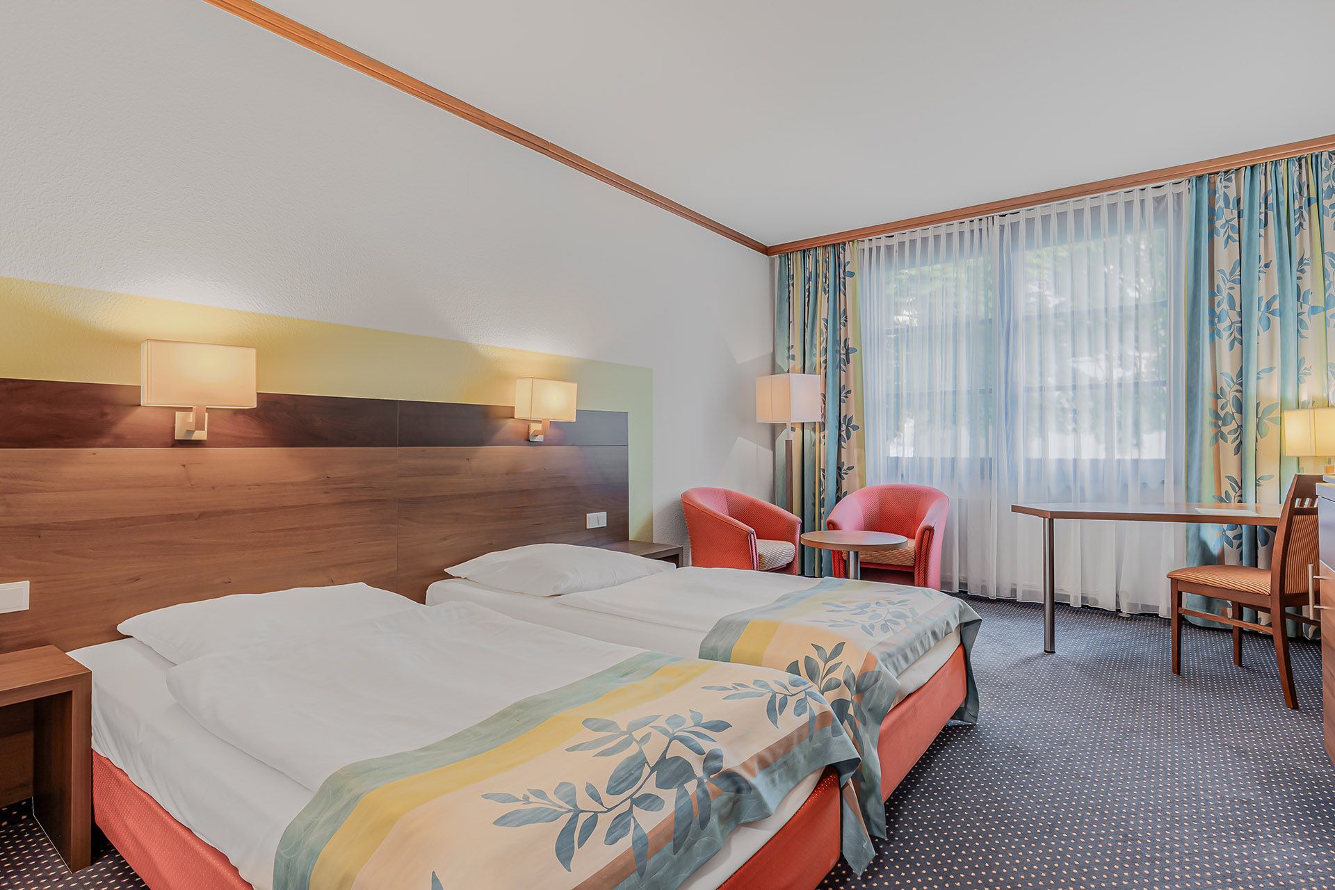 Doppelzimmer mit zwei Einzelbetten, Stühlen, Tisch und Fenster mit Vorhängen.