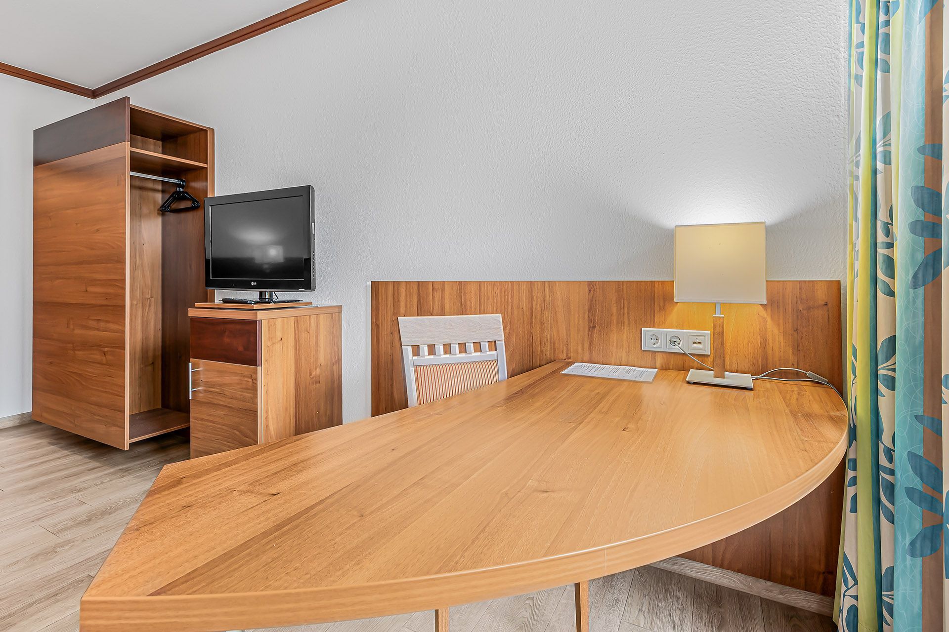 Hotelzimmer mit Schreibtisch, Fernseher, Kleiderschrank und Stuhl