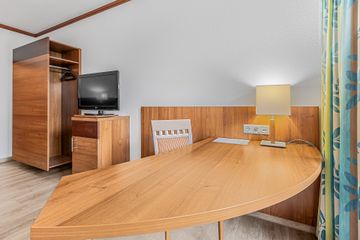 Hotelzimmer mit Schreibtisch, Fernseher, Kleiderschrank und Stuhl