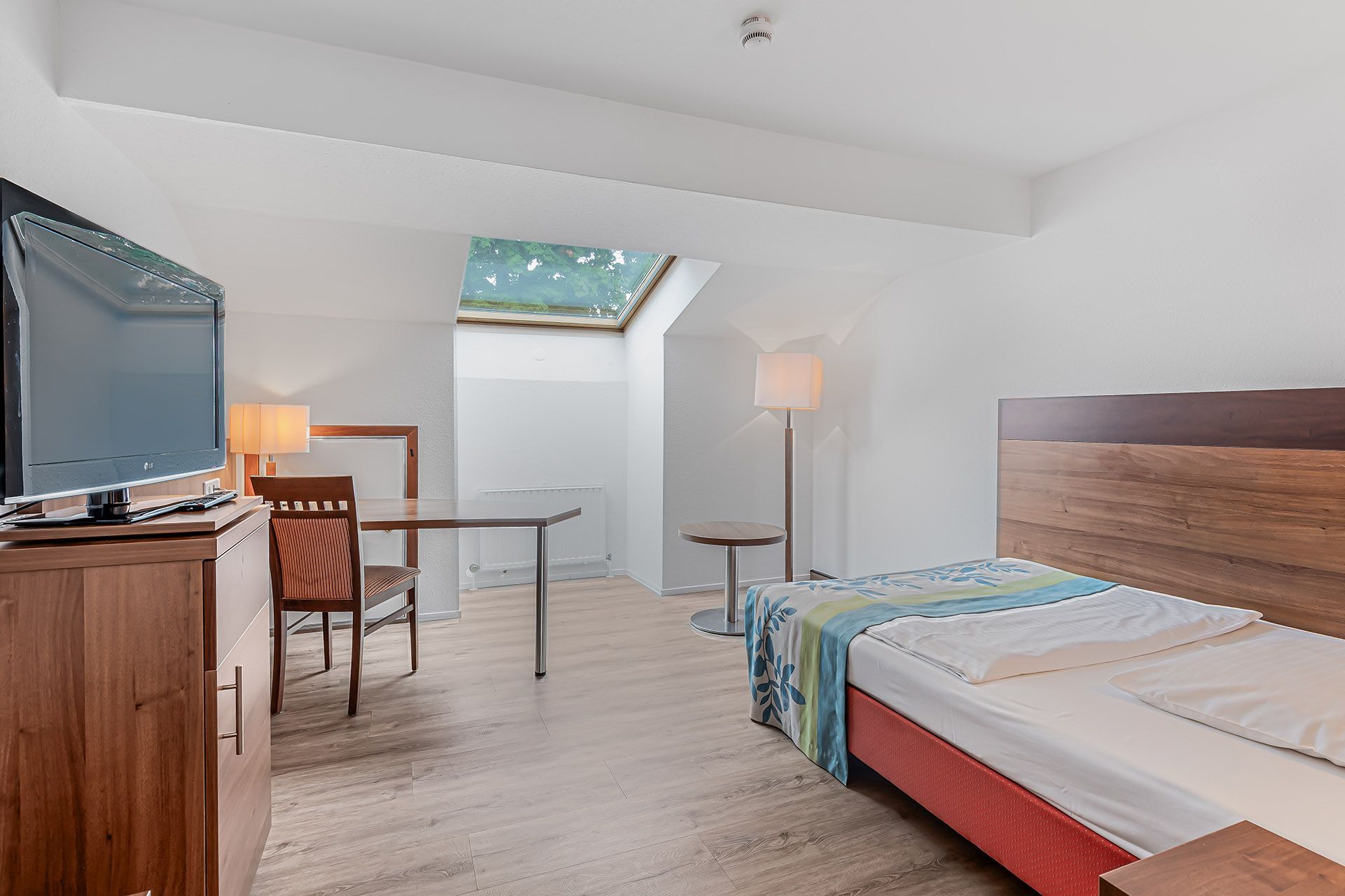 Einzelzimmer mit Bett, Schreibtisch, Fernseher und Oberlicht mit Sternenhimmel.