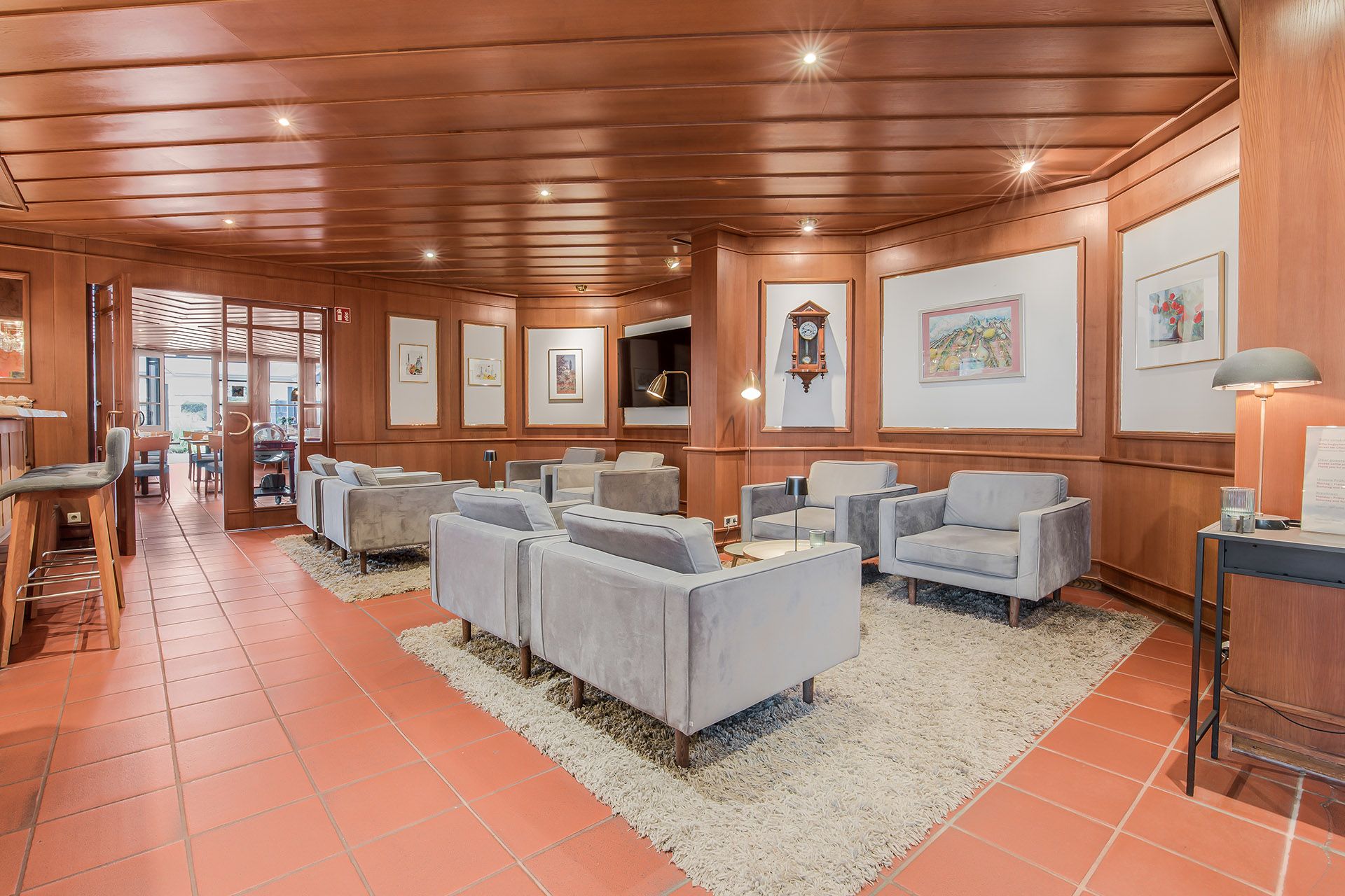 Gemütliche Lounge mit Holzvertäfelung, grauen Sofas, Kunst und Terrakottafliesenböden.