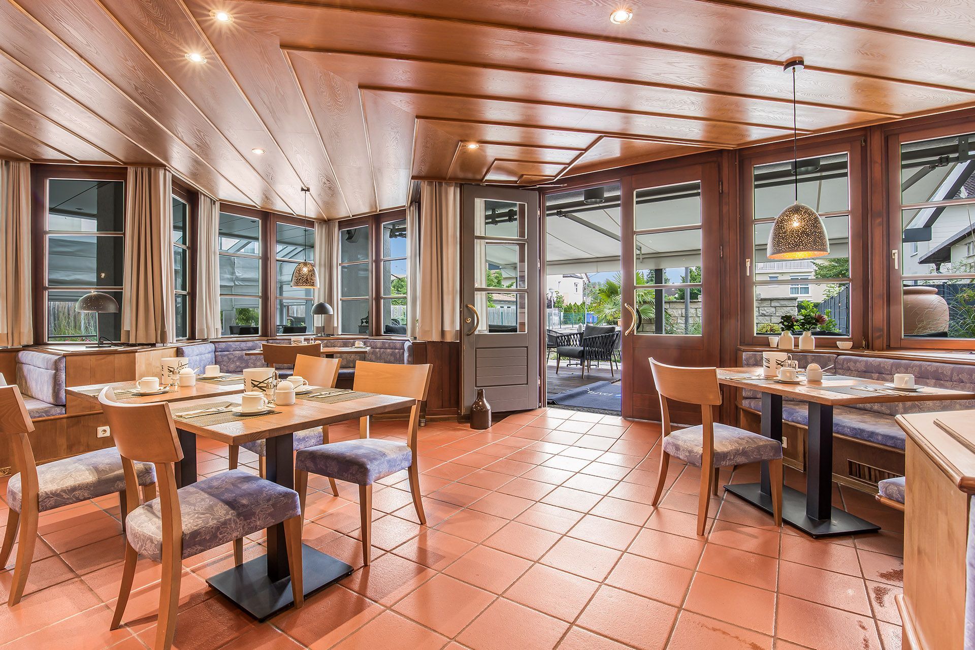 Restaurantinnenraum mit Holzwänden, gefliestem Boden, gedeckten Tischen und Blick nach draußen.