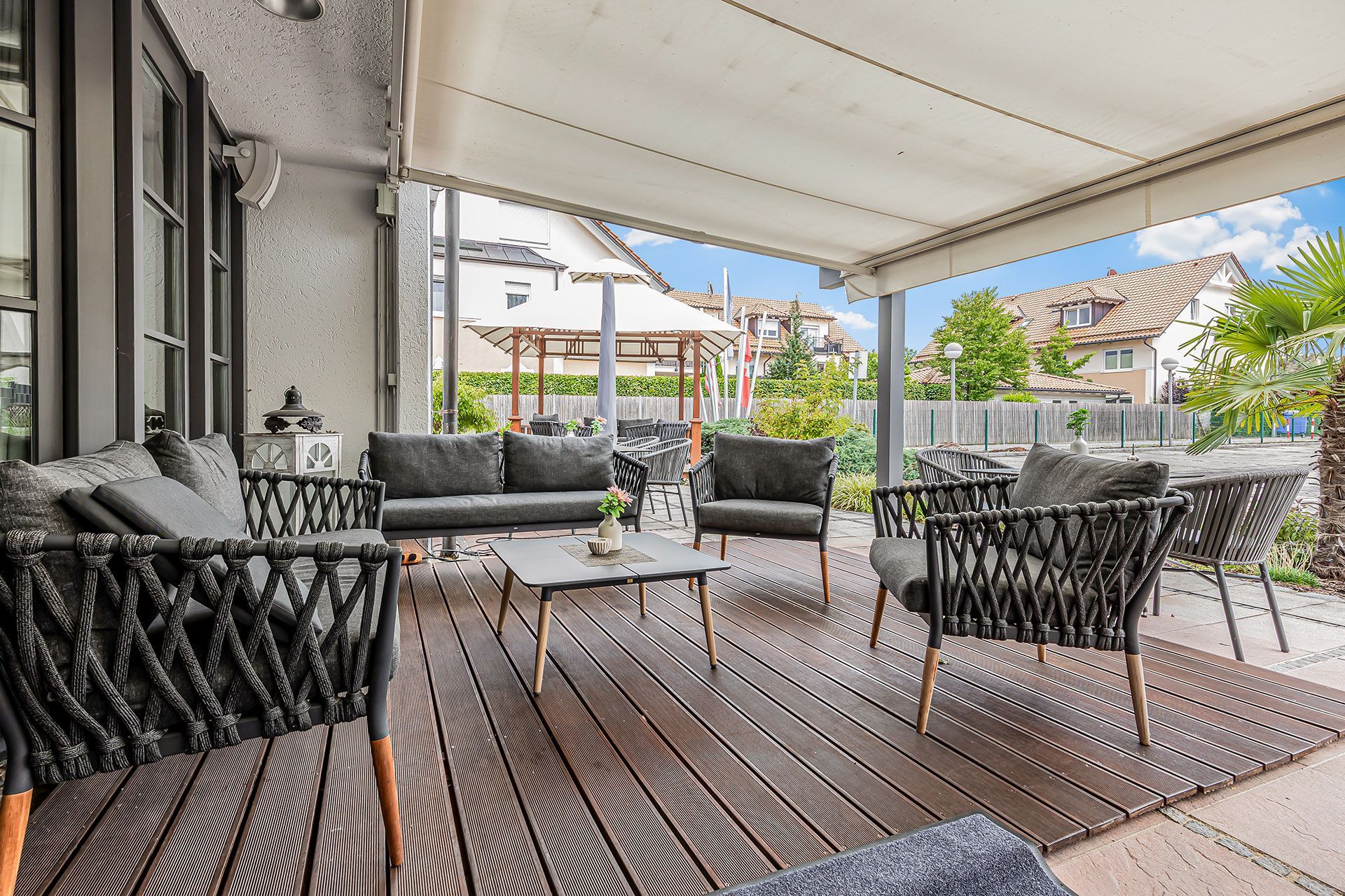 Sitzbereich auf der Außenterrasse mit grauen Möbeln, Holzdeck und einziehbarer Markise.