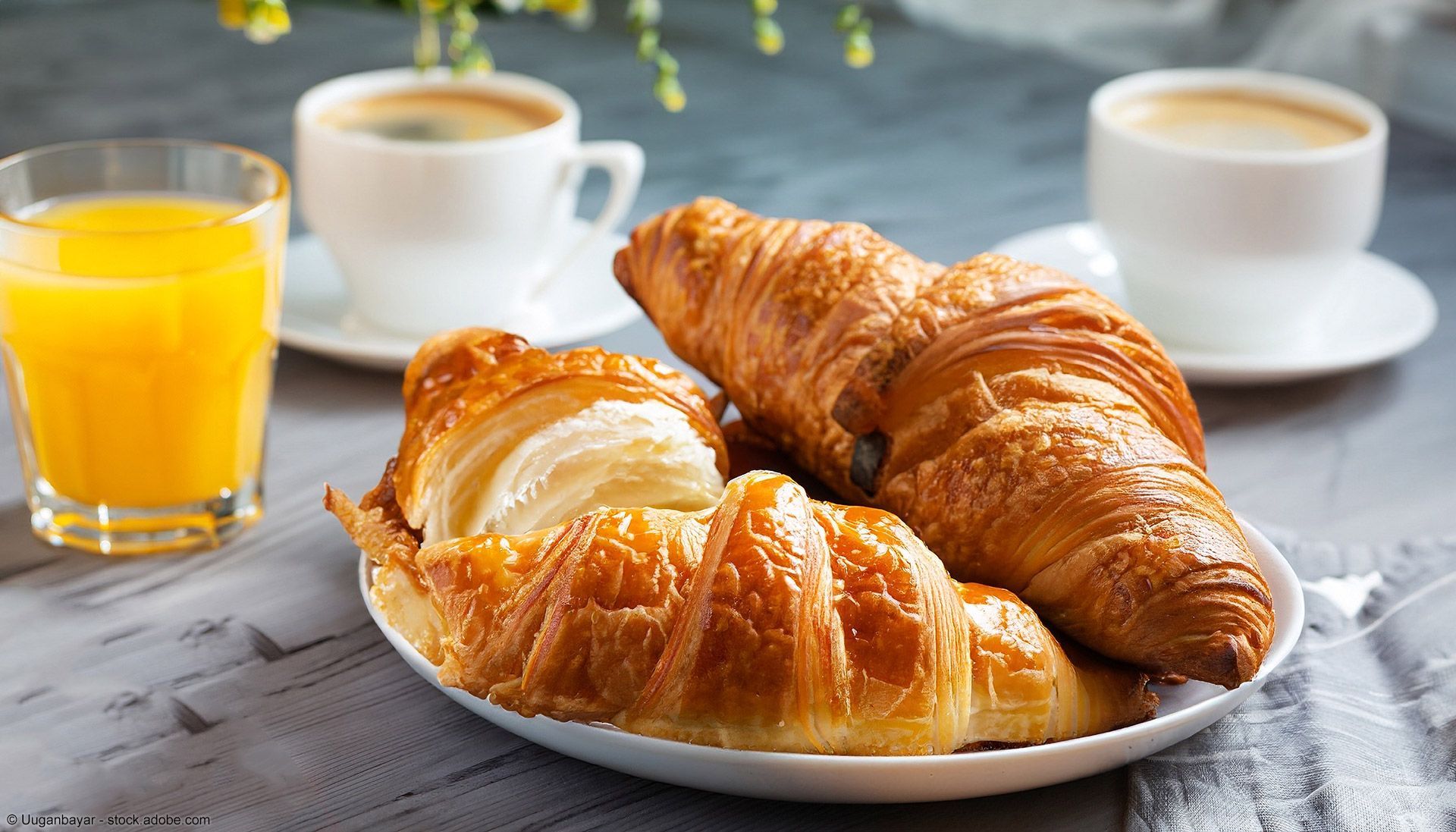 Croissants auf einem Teller, Kaffee und Orangensaft auf einem Tisch.