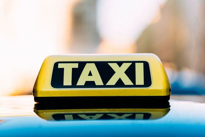 Panneau de taxi jaune sur le toit d'une voiture, arrière-plan de ville flou.