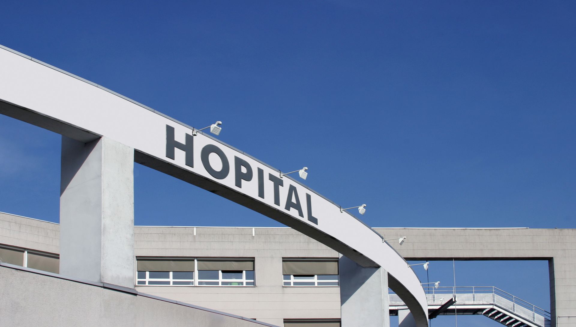 Entrée de l'hôpital avec un panneau blanc incurvé et un ciel bleu au-dessus