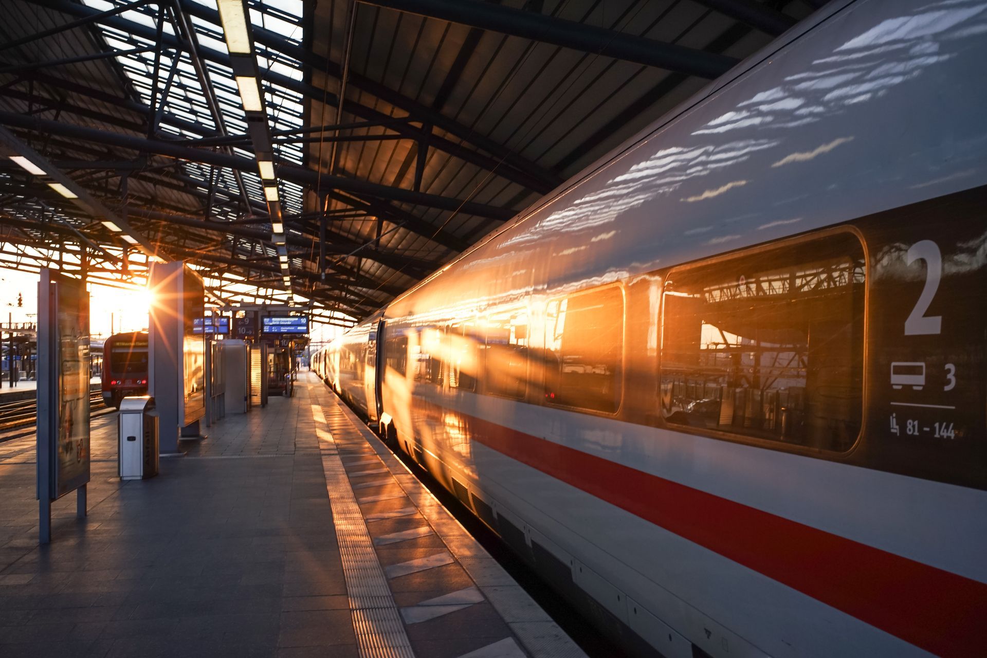 Quai de gare ensoleillé avec un train blanc et rouge sur une sous le toit couvert de la gare