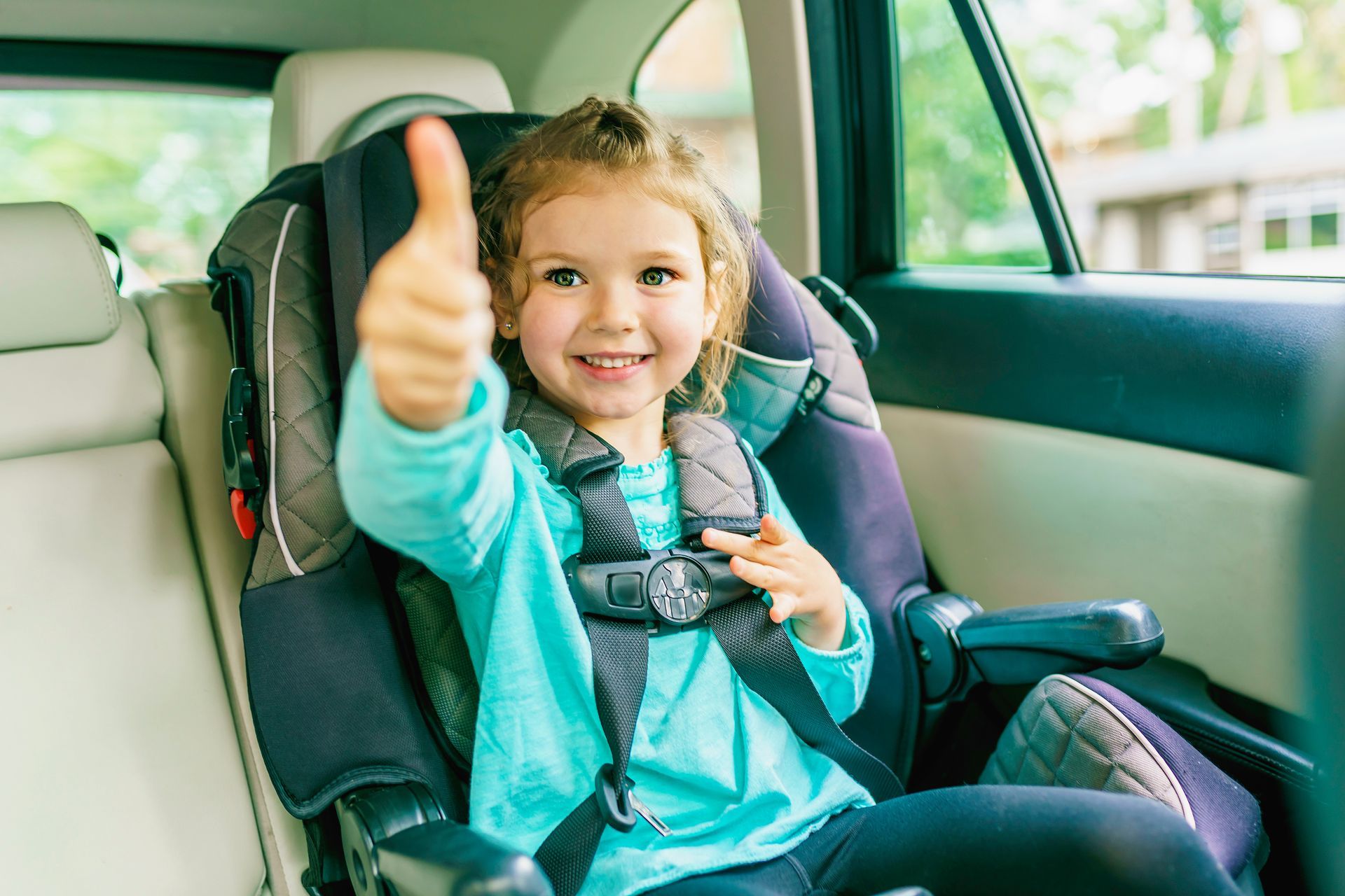 Un enfant installé dans un siège auto lève le pouce à l'intérieur d'une voiture et sourit à l'objectif.
