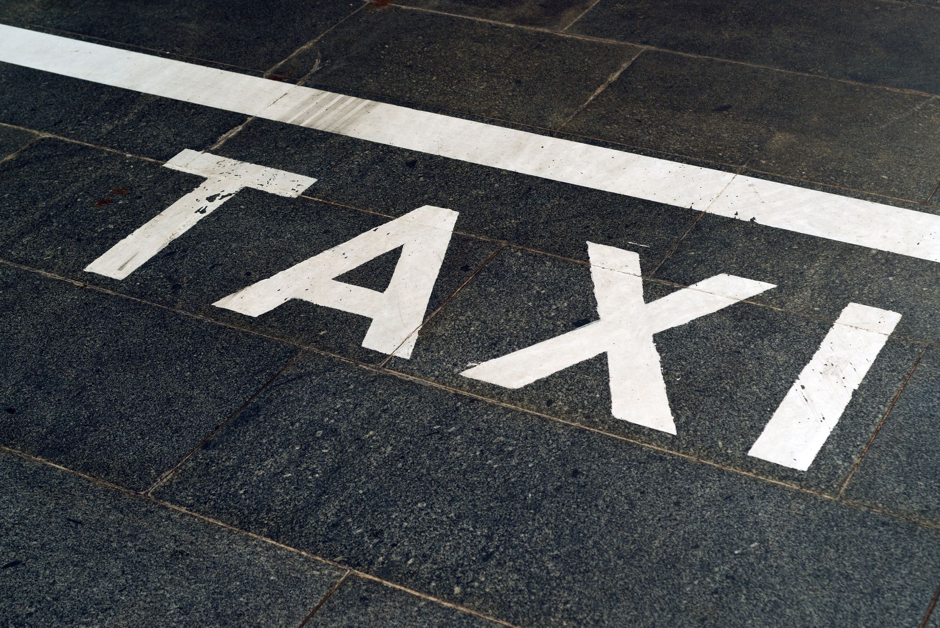 Inscription TAXI en blanc peinte sur une chaussée en asphalte foncé.