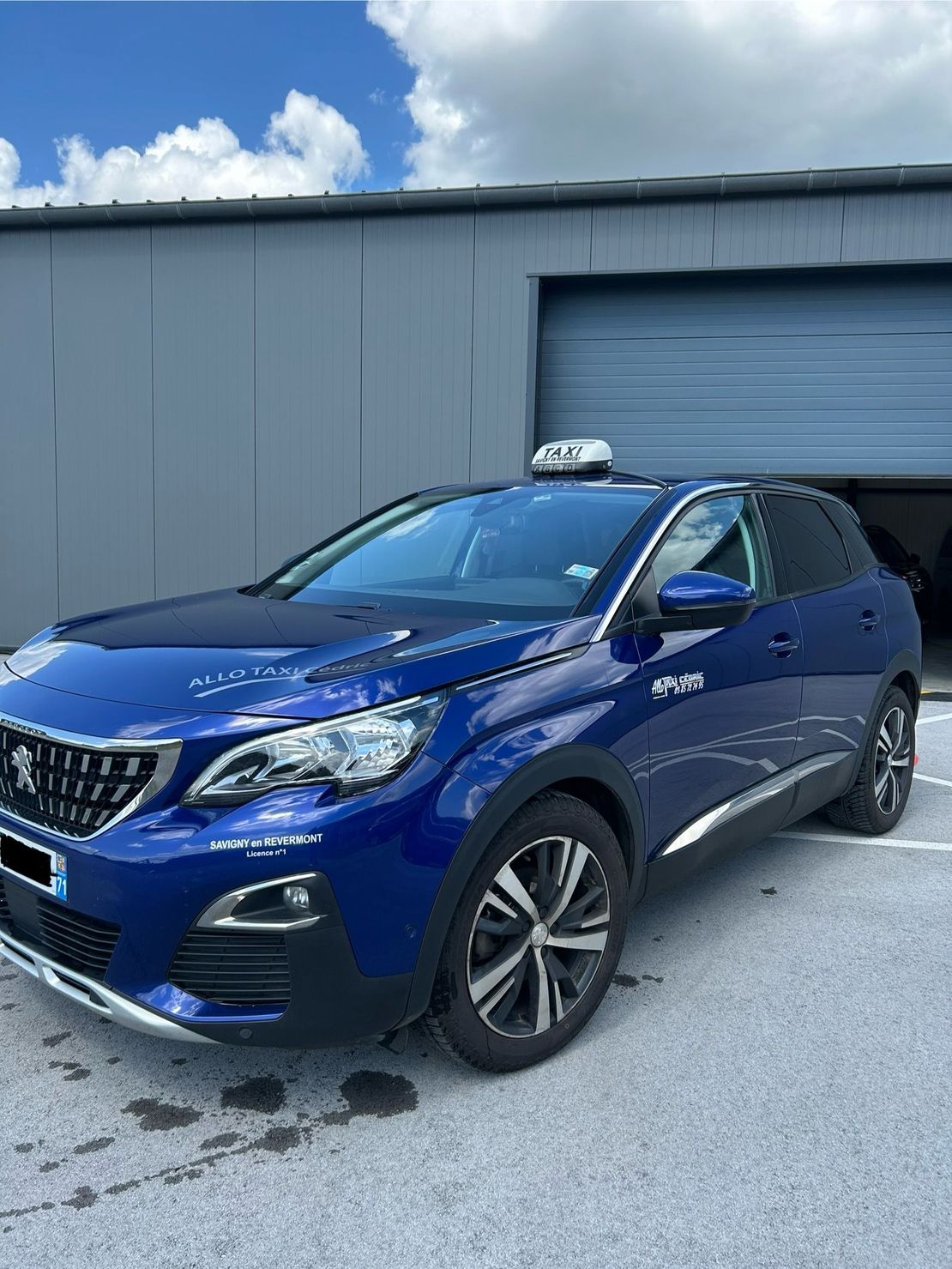 Un SUV bleu garé à côté d'un garage gris sous un ciel partiellement nuageux.