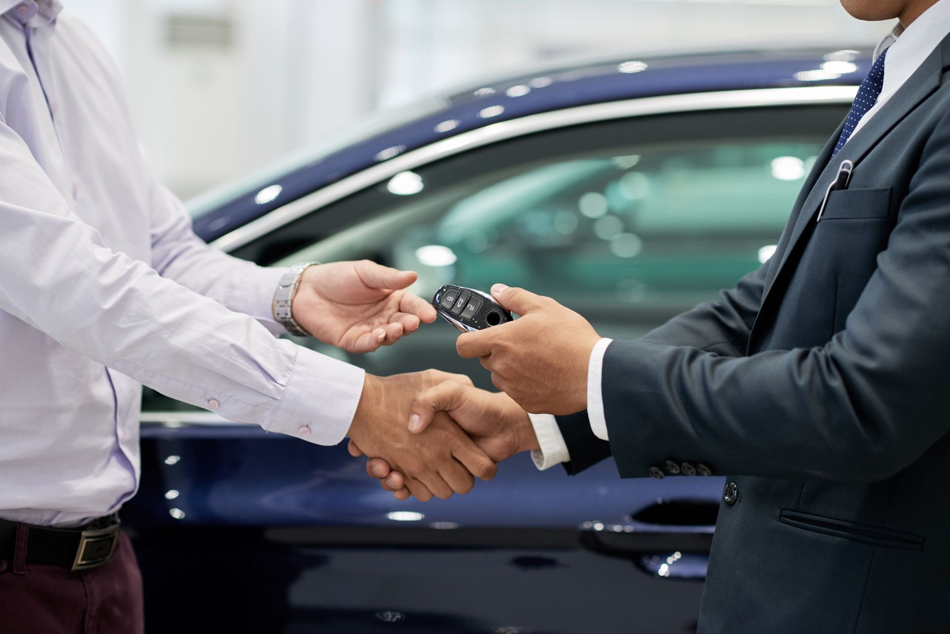 Deux hommes en costume se serrent la main au sujet de clés de voiture à côté d'une voiture bleue.