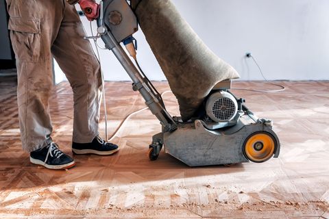 Un hombre está lijando un piso de madera con una máquina.