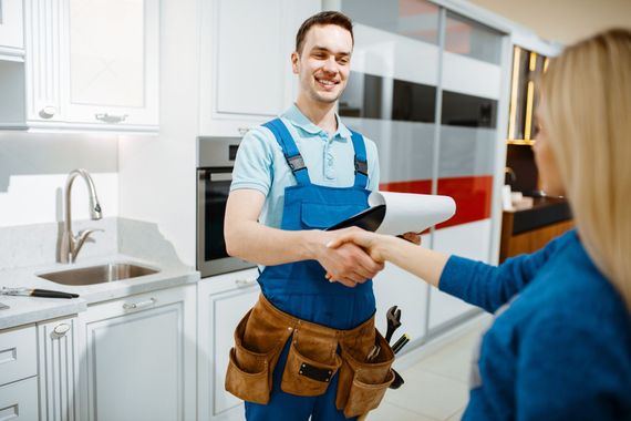 Un hombre con mono le estrecha la mano a una mujer en una cocina.