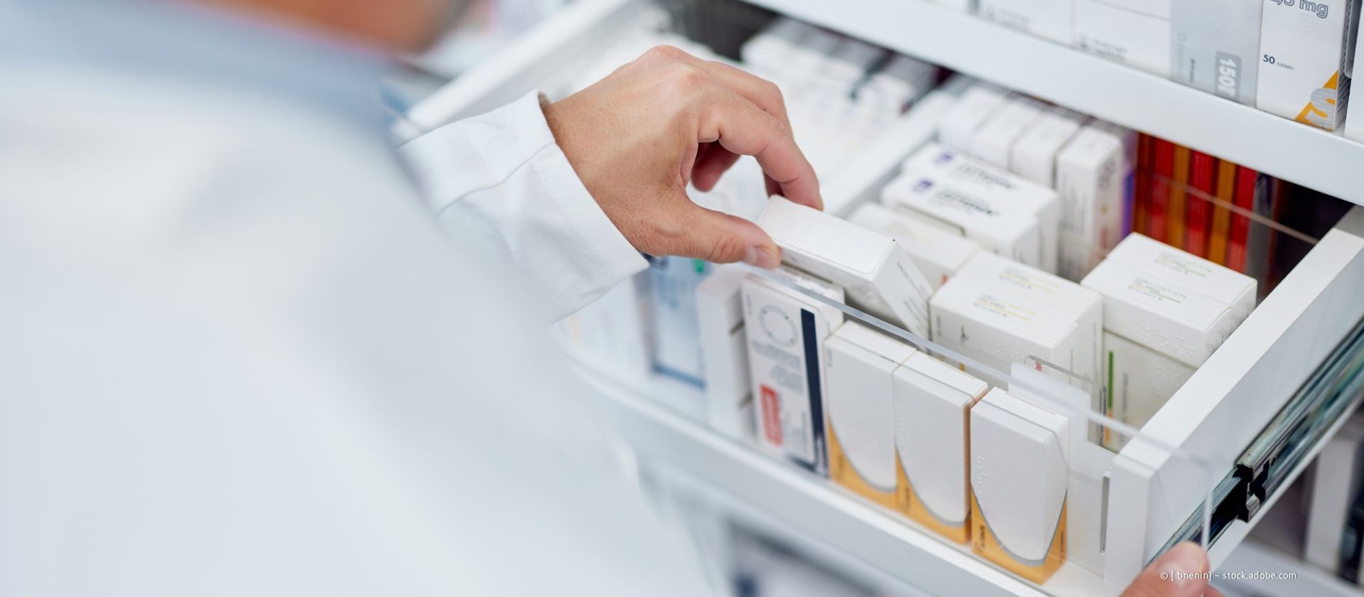 Eine Person im weißen Kittel greift in eine Schublade voller Medikamentenpackungen.