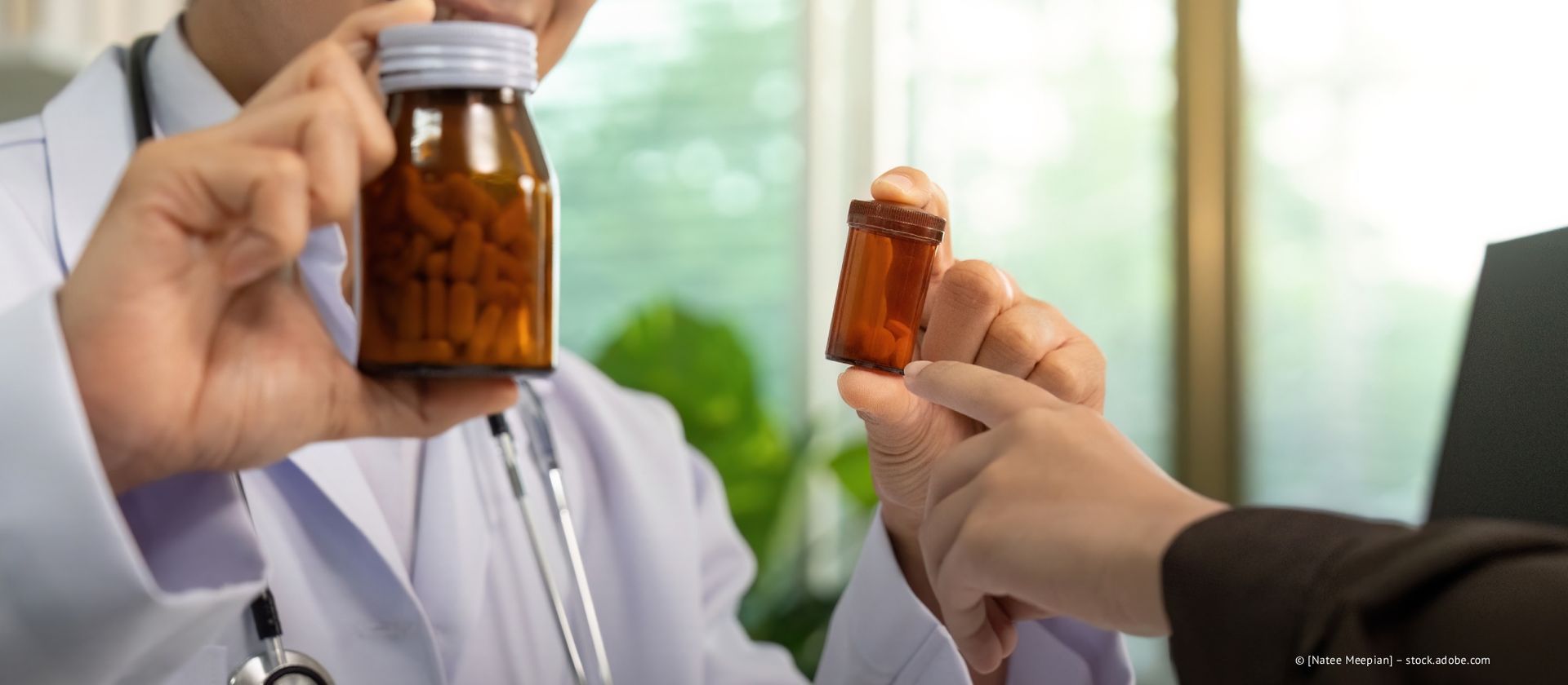 Ein Arzt im weißen Kittel hält eine Flasche mit Pillen in der Hand und bietet einem Patienten eine kleinere Flasche an. Sie befinden sich in einem gut beleuchteten Büro.