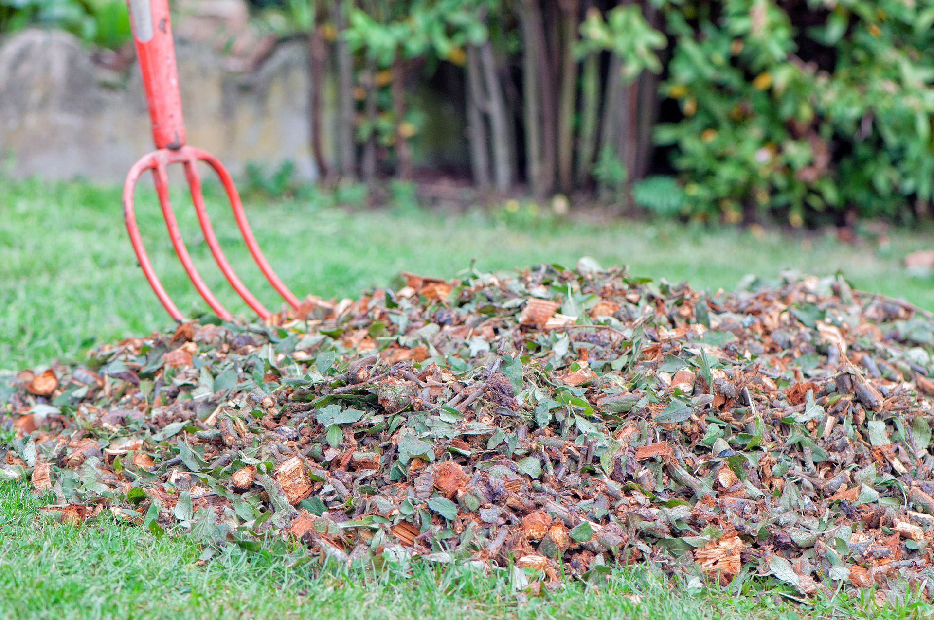 Un tas de déchets verts avec une fourche rouge sur une pelouse.