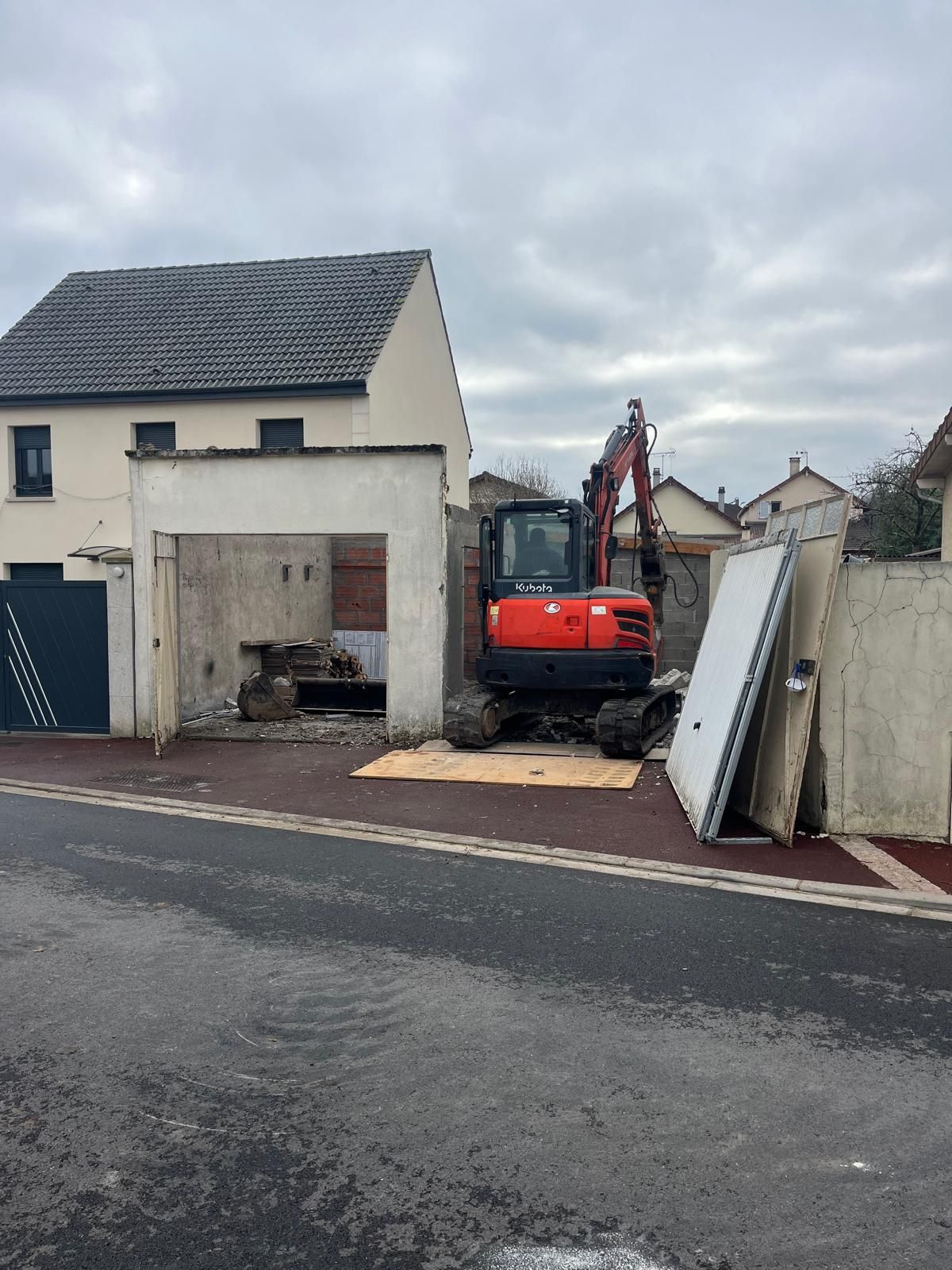 Une pelleteuse démolit une structure en béton à côté d'une maison.
