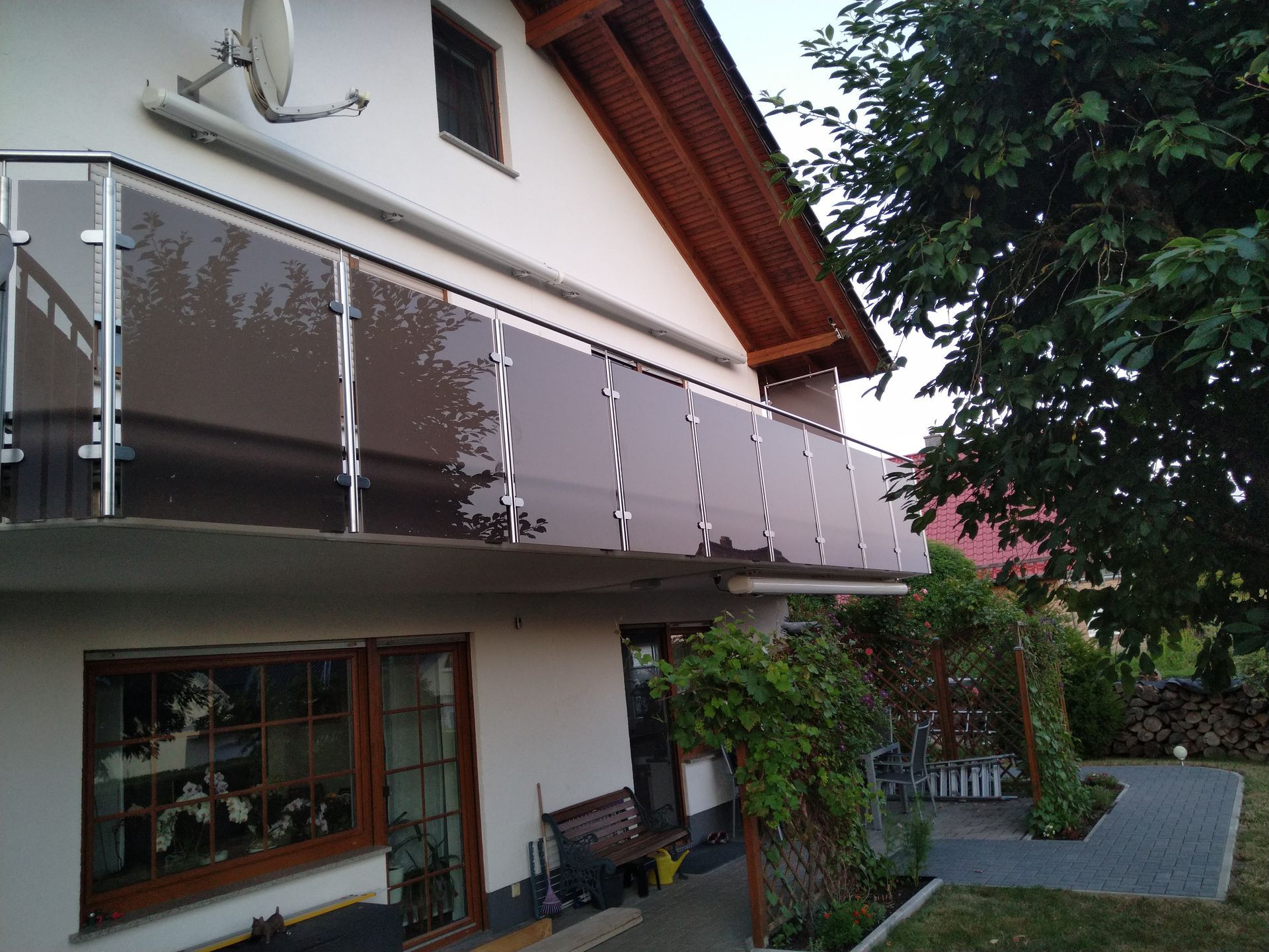 Hausfassade mit Glasbalkon und Gartenweg unter einem Holzdach