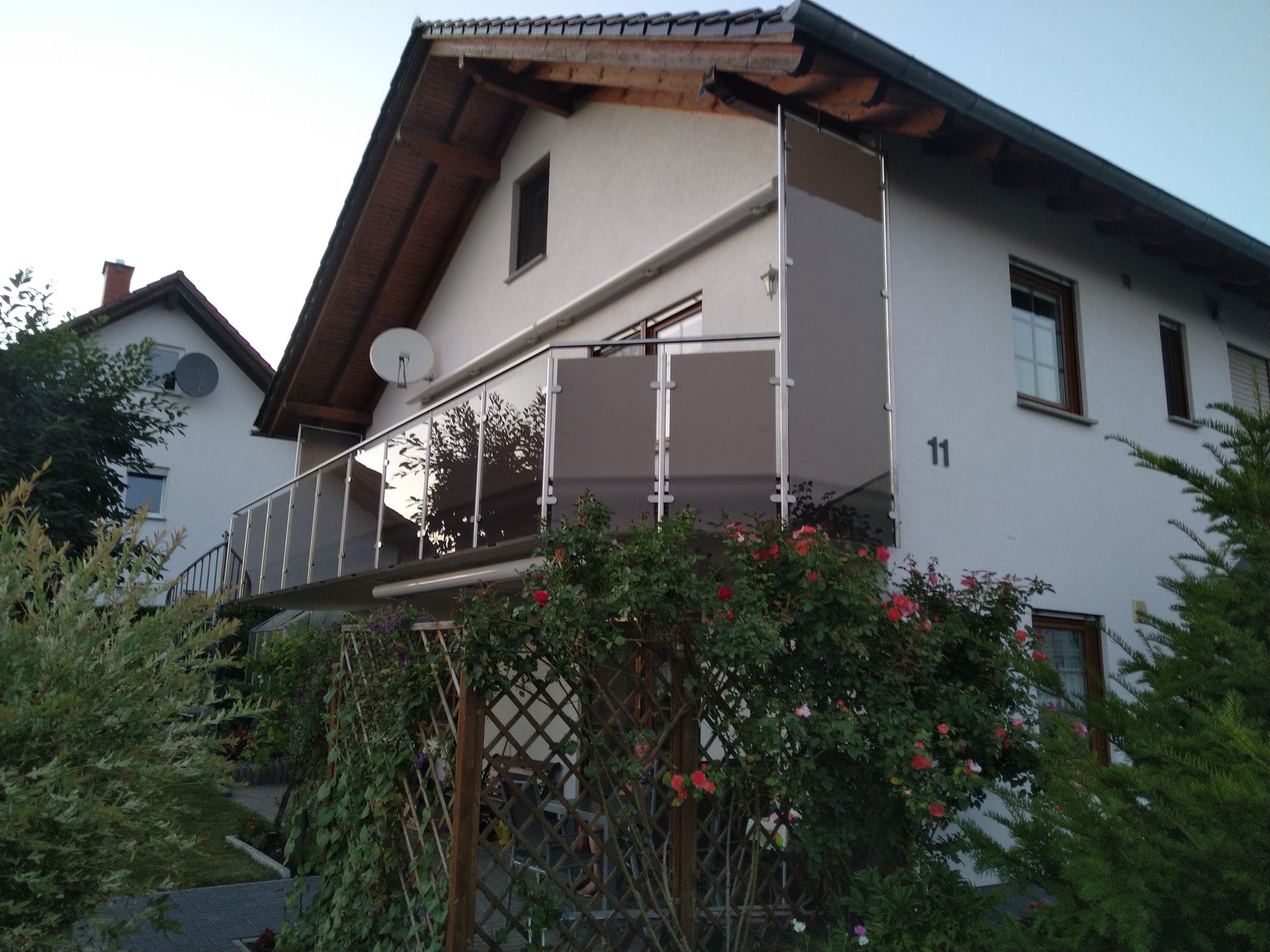 Weißes Haus mit Balkon und Garten, von außen gesehen.