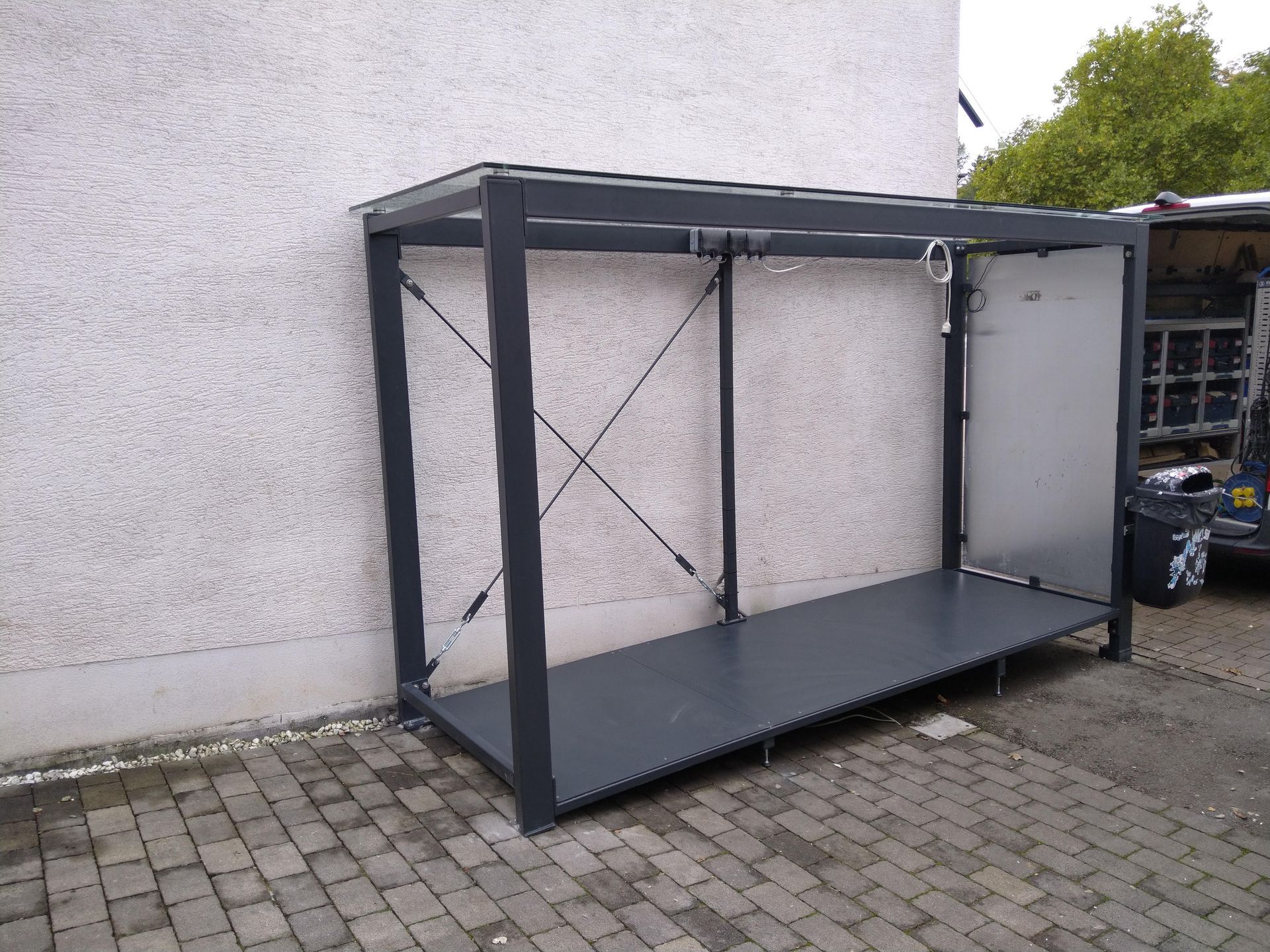 Auf einem gepflasterten Gehweg vor einem Gebäude steht eine Metallkonstruktion.