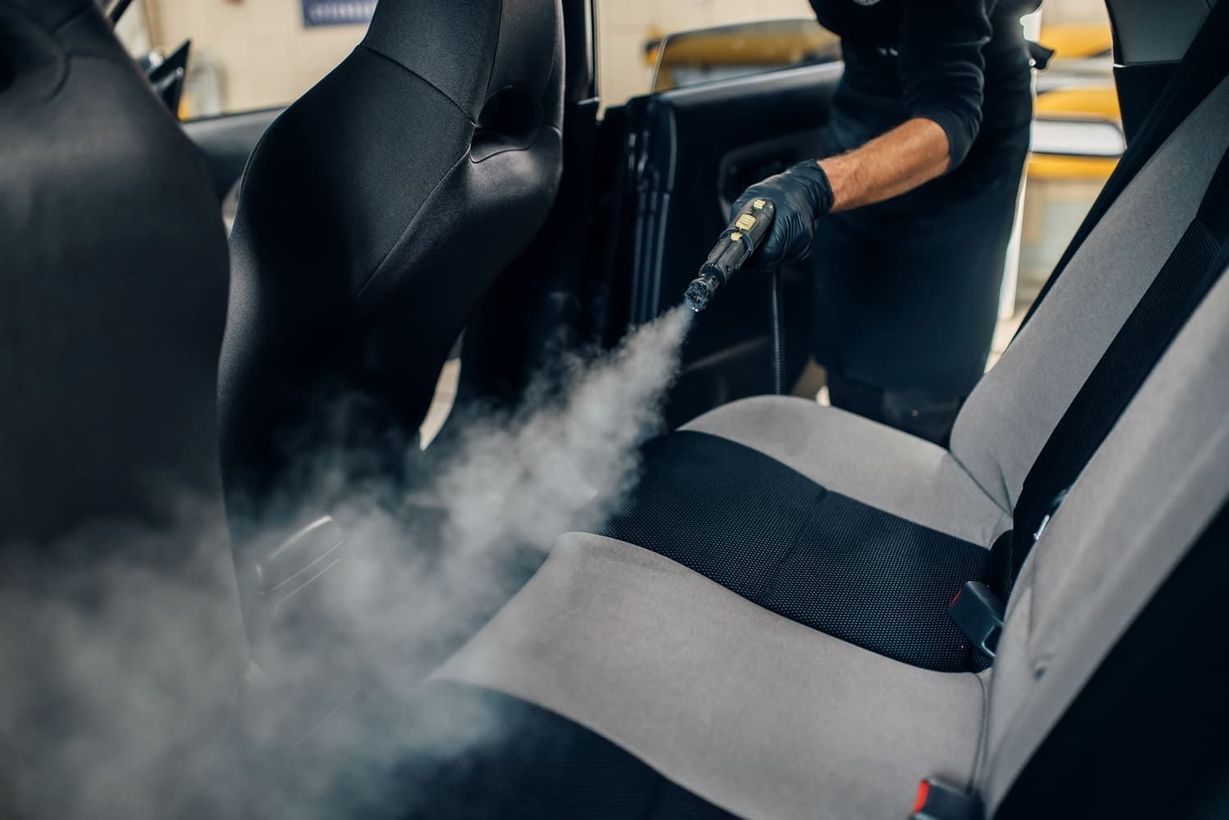 Un hombre está limpiando los asientos de un coche con un limpiador a vapor.