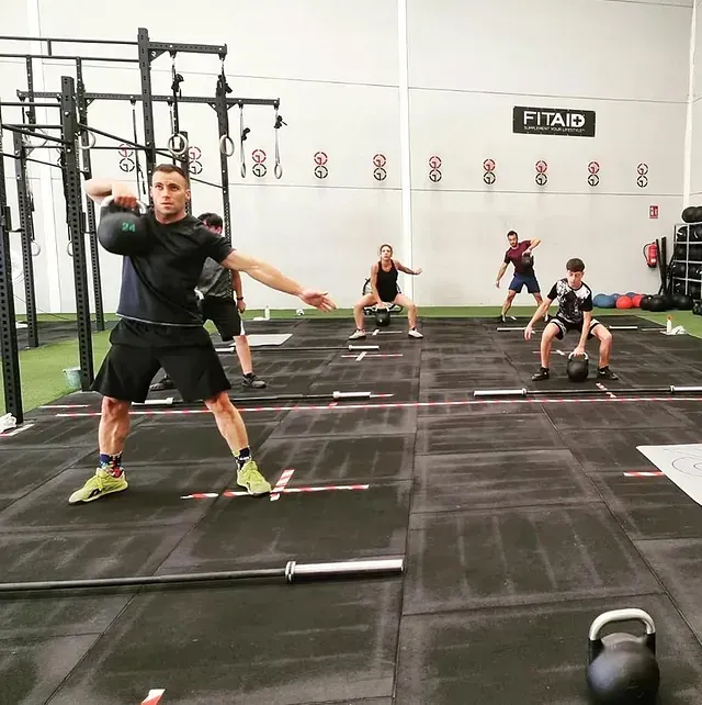 Un grupo de personas está haciendo ejercicio en un gimnasio con un cartel que dice fitaid