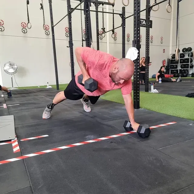 Un hombre está haciendo flexiones con mancuernas en un gimnasio.