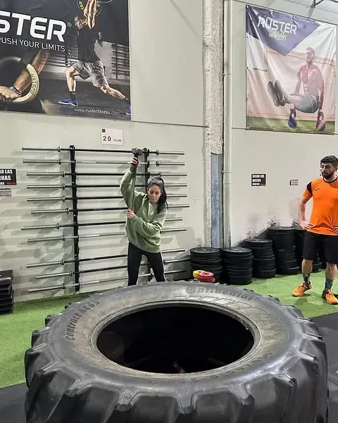 Una mujer está parada junto a un neumático grande en un gimnasio.