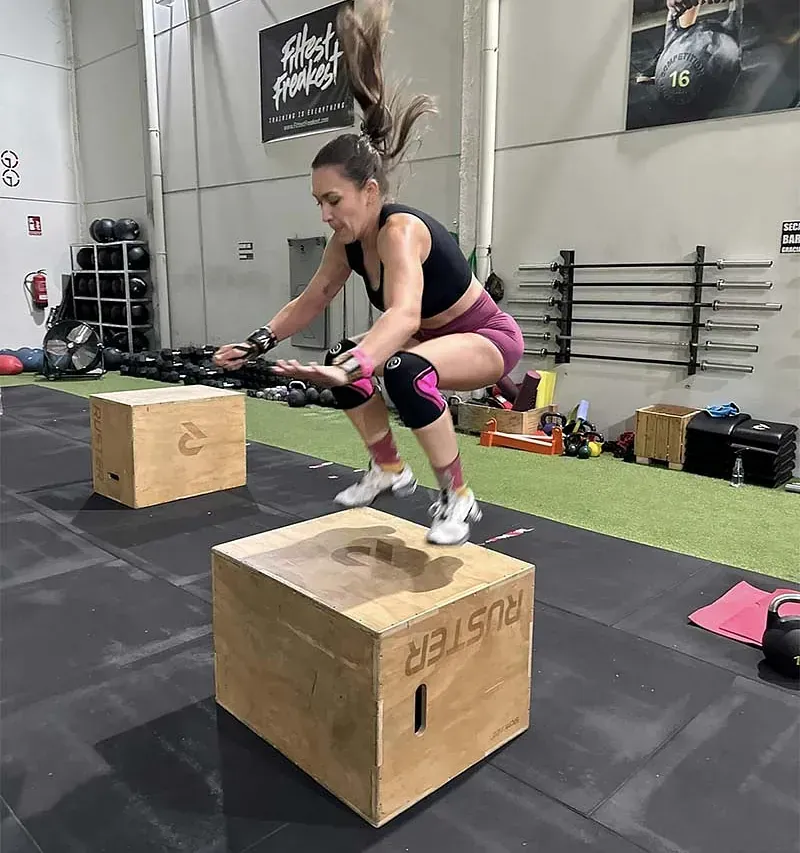 Una mujer está en cuclillas sobre una caja de madera en un gimnasio.