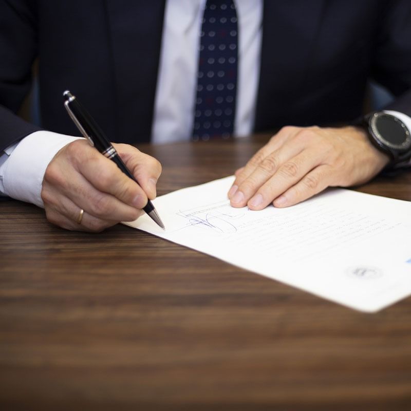 Un hombre con traje y corbata está escribiendo en un trozo de papel con un bolígrafo.