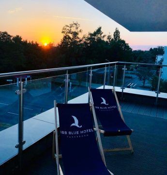 Zwei blaue Liegestühle auf einem Balkon mit einem Sonnenuntergang im Hintergrund