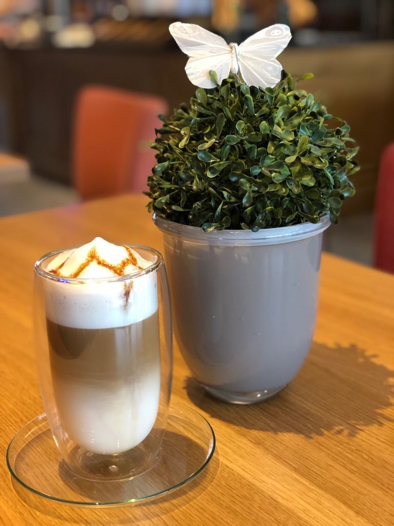 Eine Tasse Kaffee neben einer Topfpflanze mit einem Schmetterling darauf