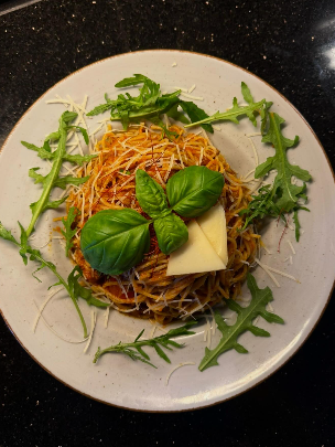 Spaghetti mit roter Sauce, garniert mit Käse, Basilikum und Rucola auf einem weißen Teller.