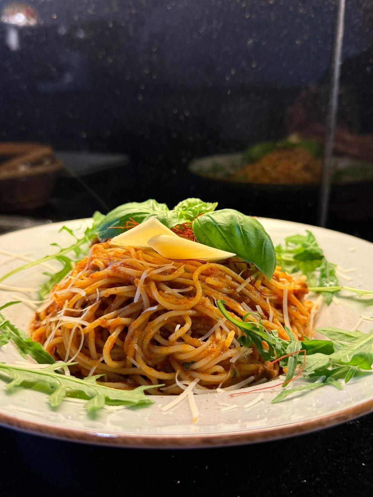 Spaghetti mit roter Sauce, Basilikum, Parmesan und Rucola auf einem Teller.