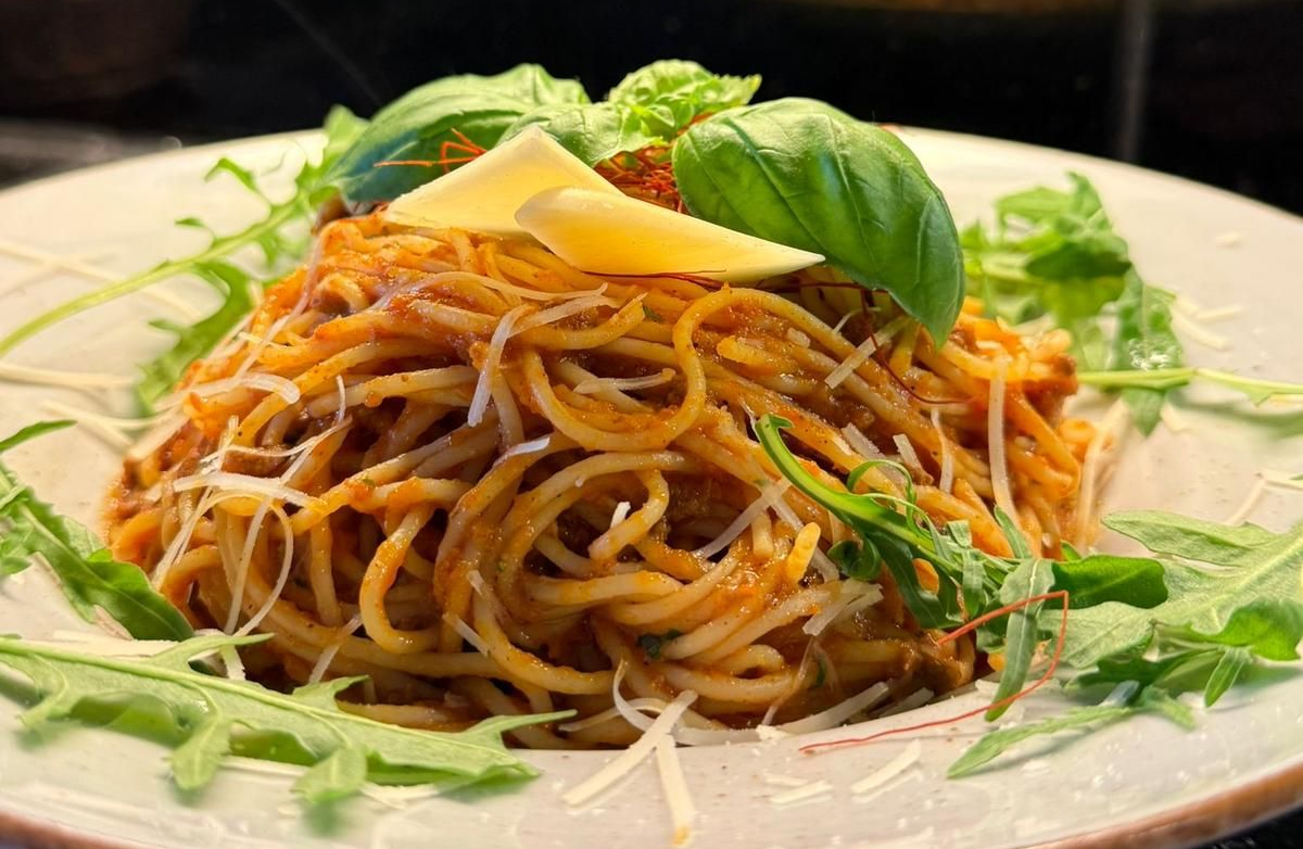 Spaghetti mit Tomatensoße, Rucola, Basilikum, Käse und Butter auf einem weißen Teller.