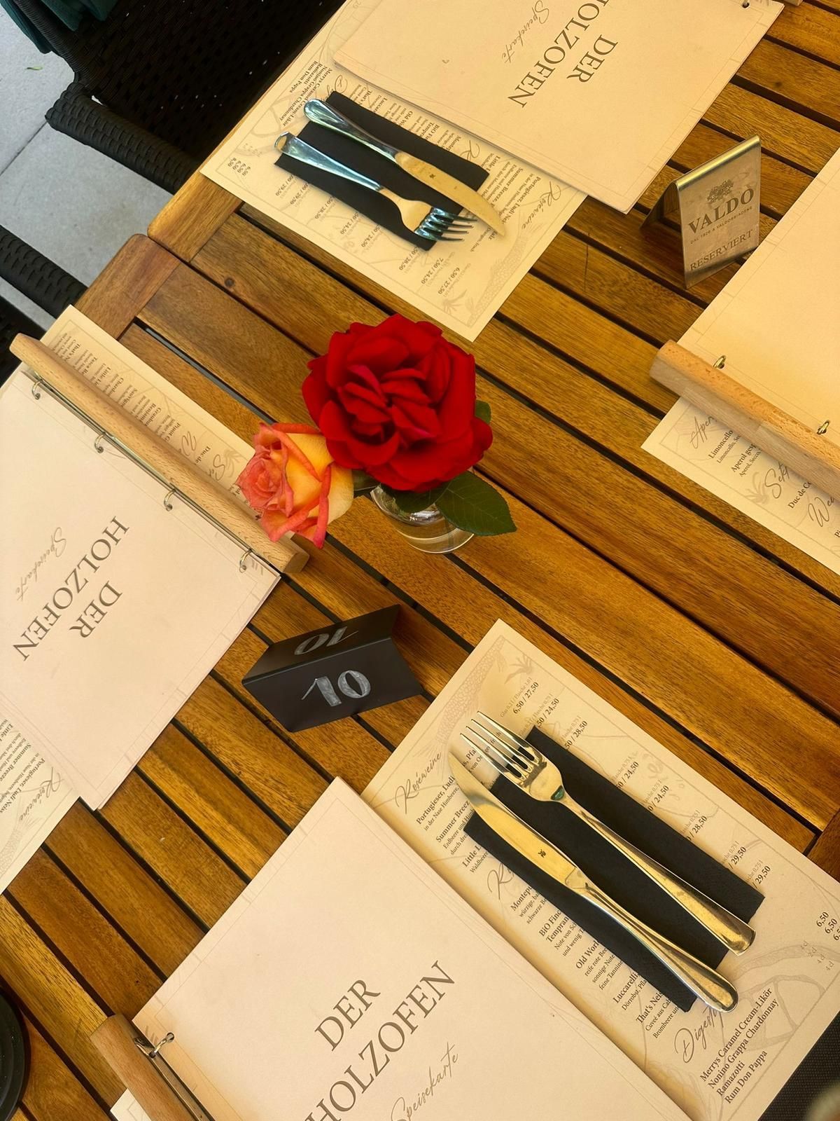 Tischgedeck in einem Restaurant mit Speisekarten, Besteck, einer Rose und einer Tischnummer.