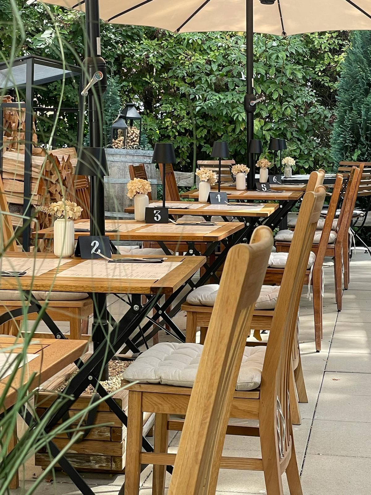 Sitzplätze im Restaurant im Freien mit Holztischen, Stühlen und Sonnenschirmen, umgeben von Grün.