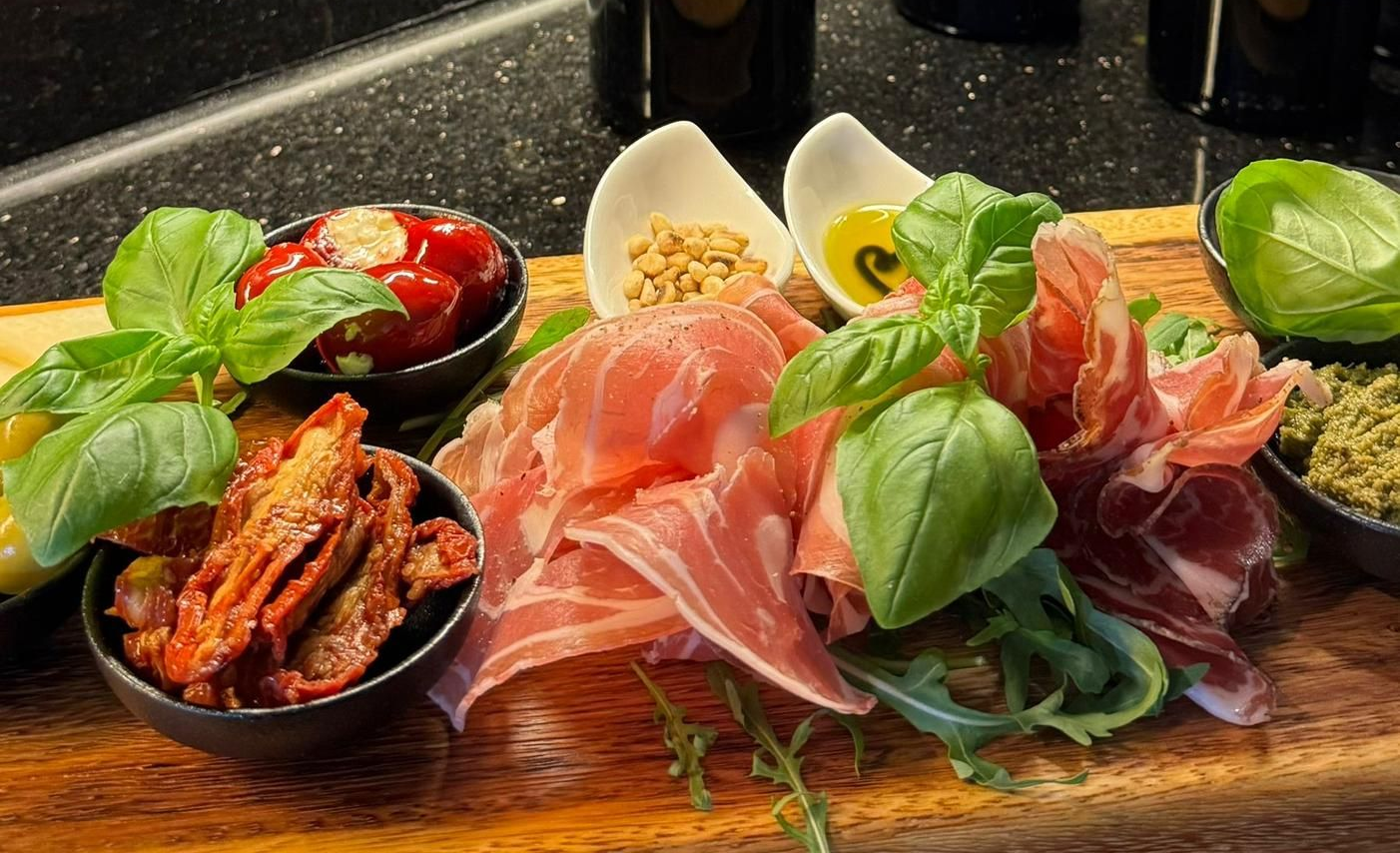 Wurstplatte mit Prosciutto, sonnengetrockneten Tomaten, Paprika, Nüssen, Pesto, Basilikum und Olivenöl.
