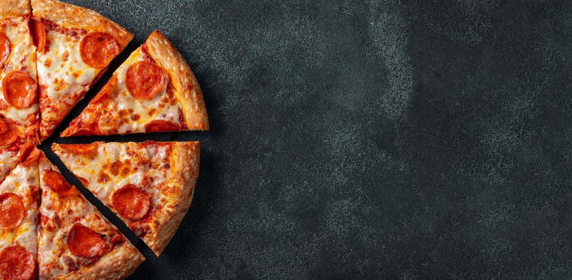 Mehrere geschnittene Pepperoni-Pizzastücke auf einer dunklen, strukturierten Oberfläche.