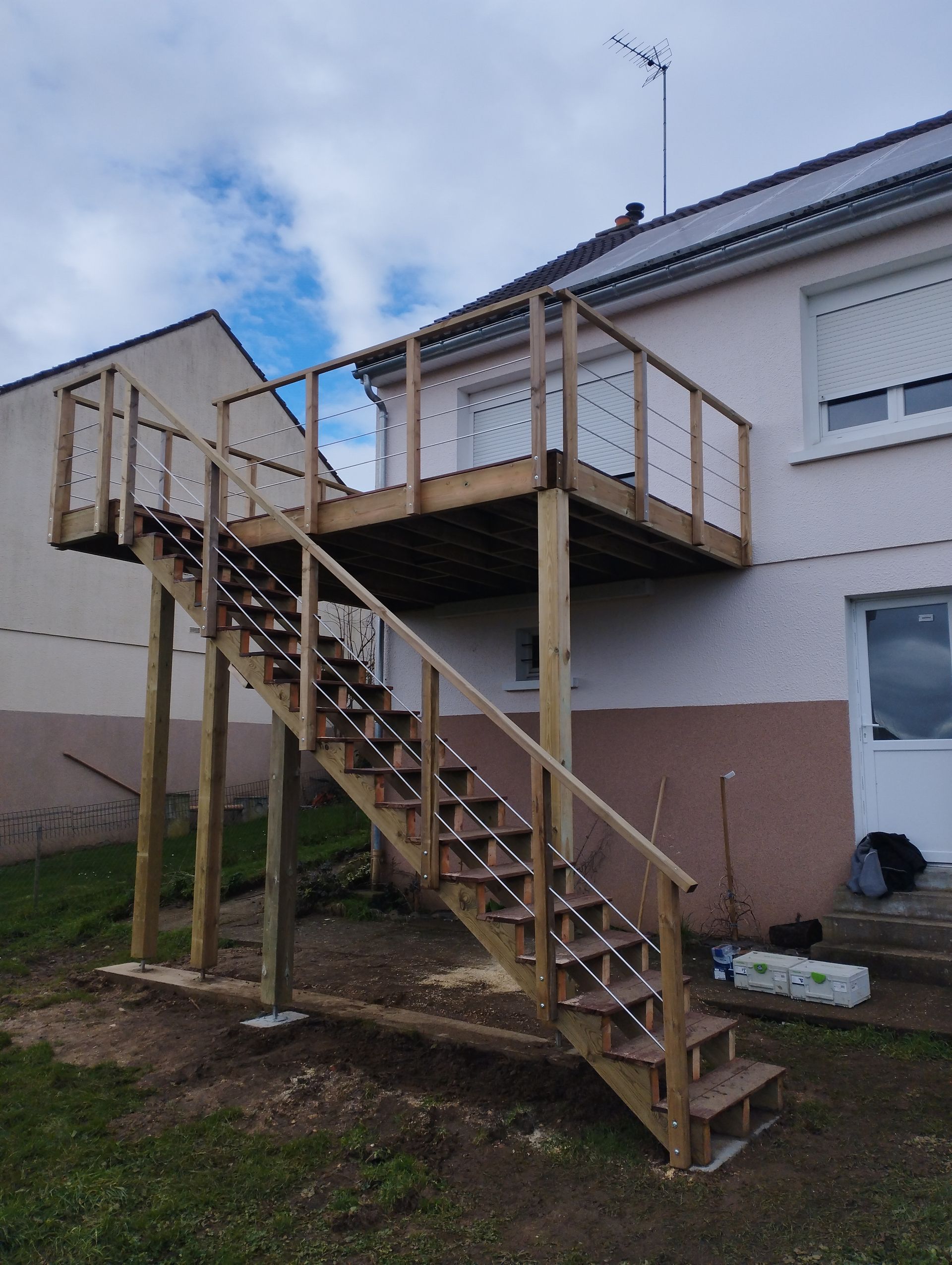 Terrasse sur pilotis avec un escalier en bois attenants à une maison