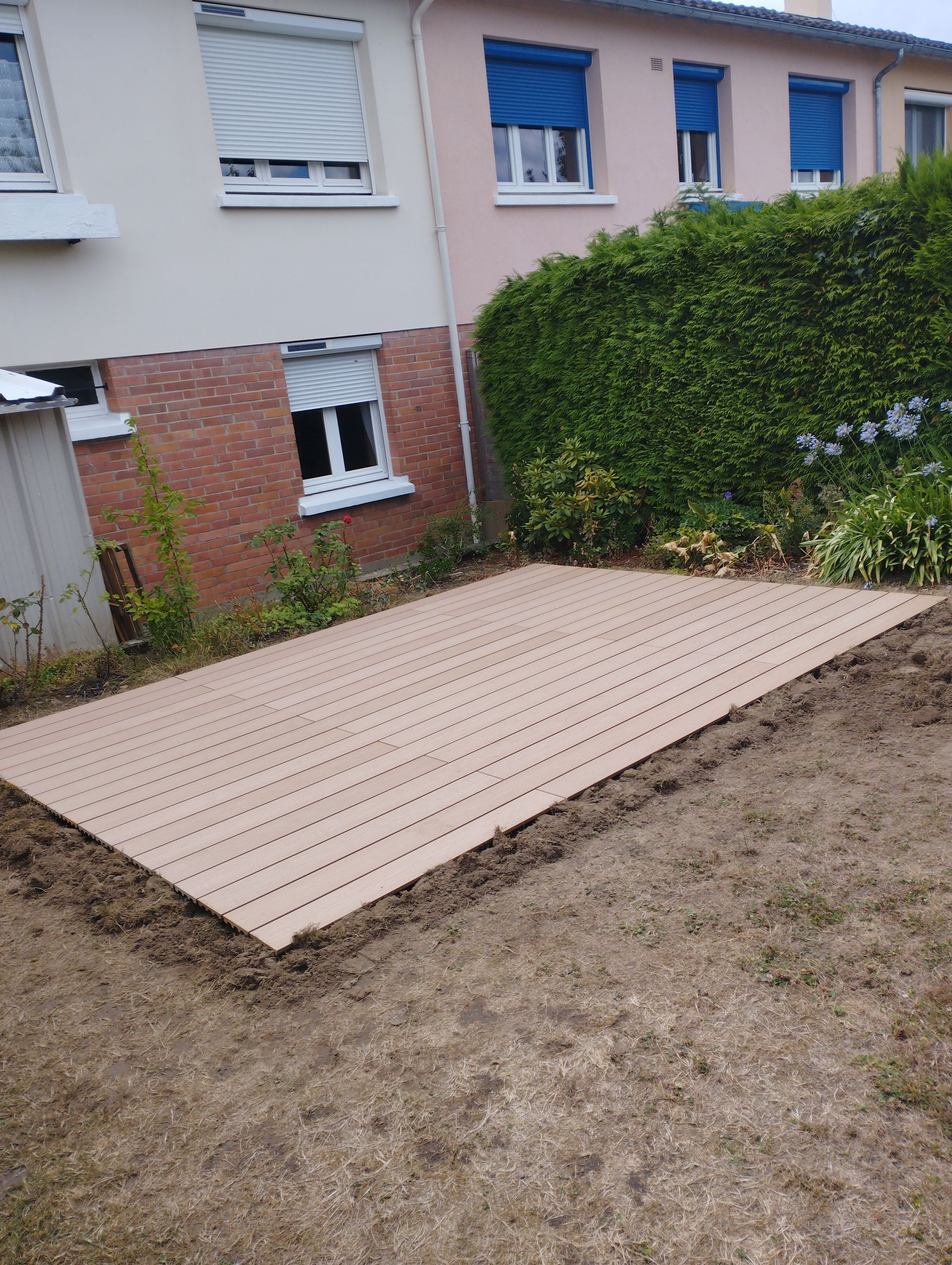 Une terrasse composite rectangulaire qui borde une maison en brique et une  haie végétale