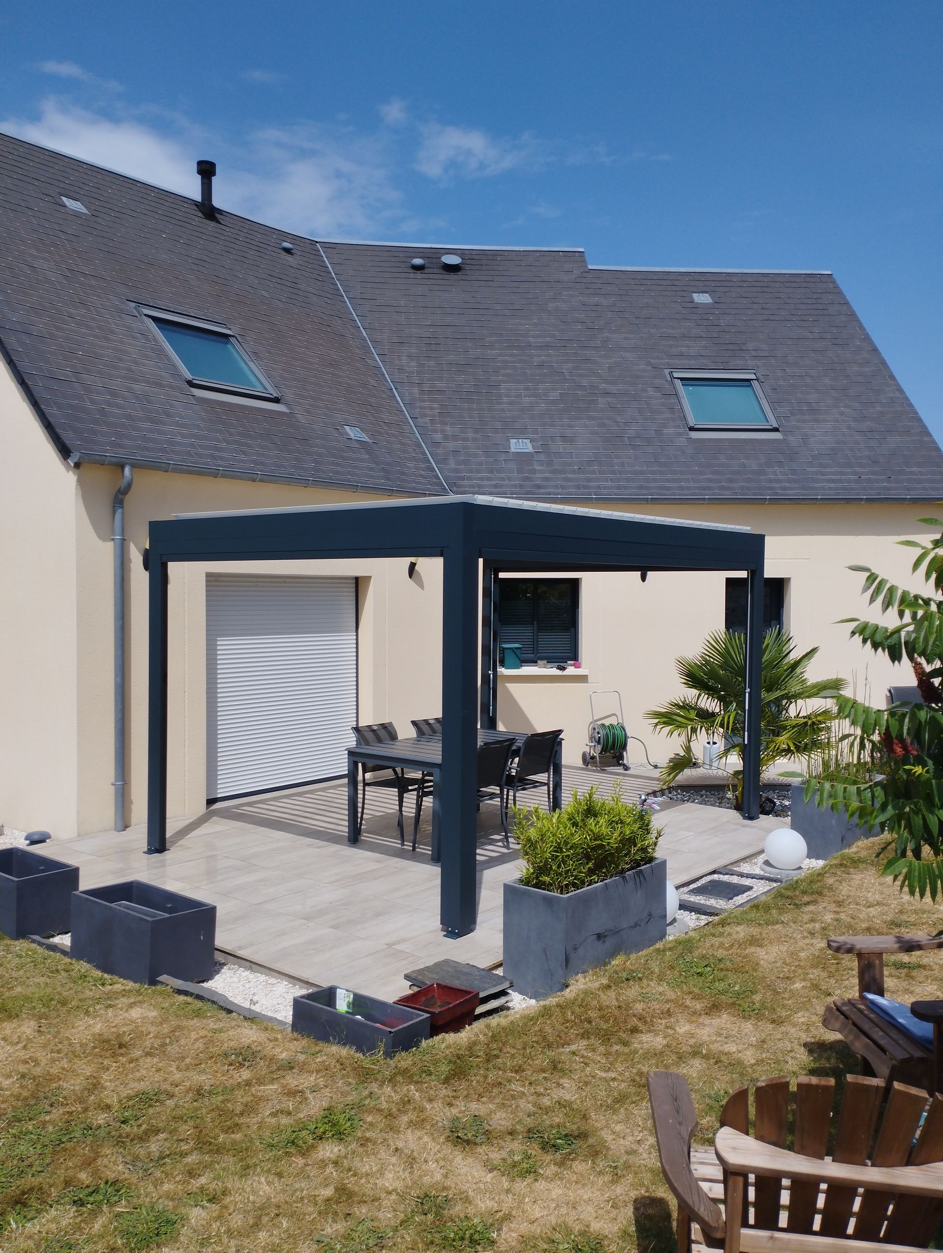 Maison beige avec une pergola gris foncé au-dessus d'une terrasse