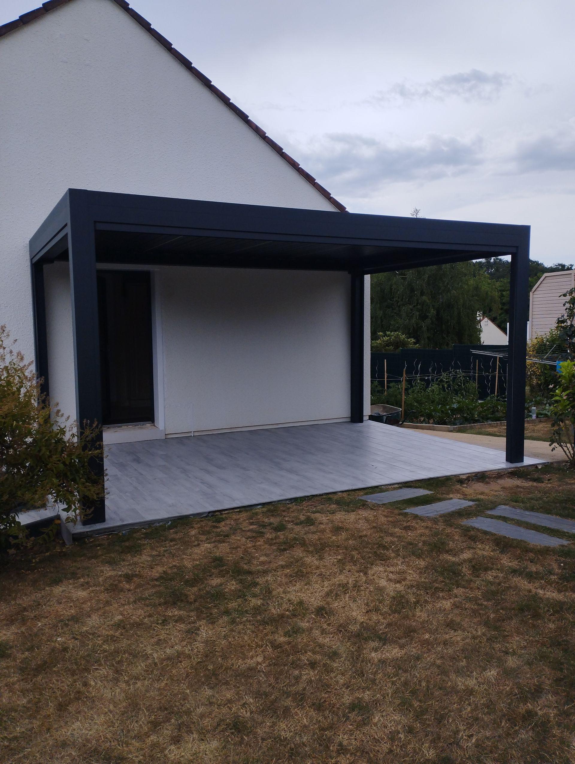 Pergola adossée à une maison blanche avec terrasse carrelée de gris