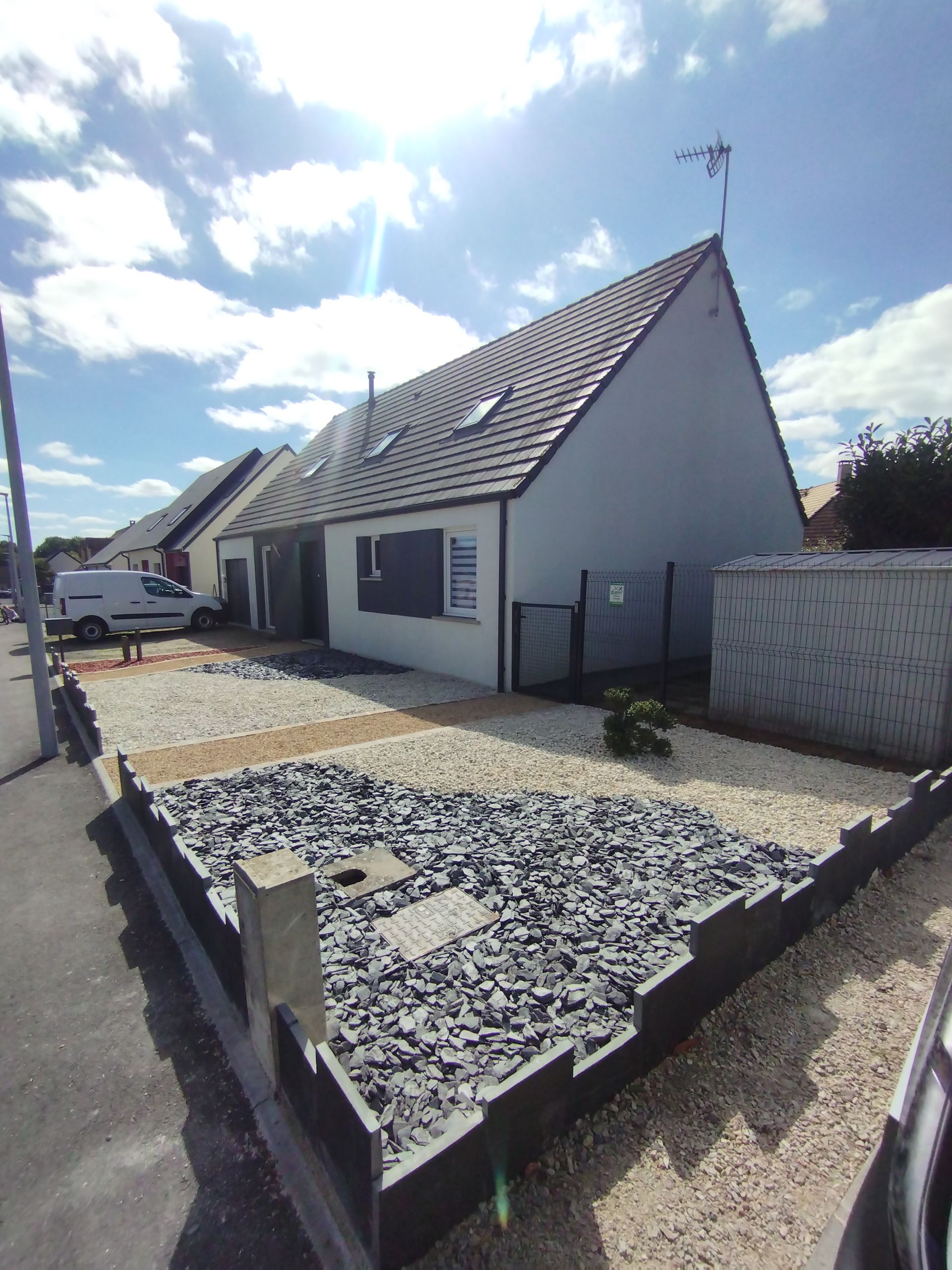 Maison avec toit gris, murs blancs et cour recouverte de graviers